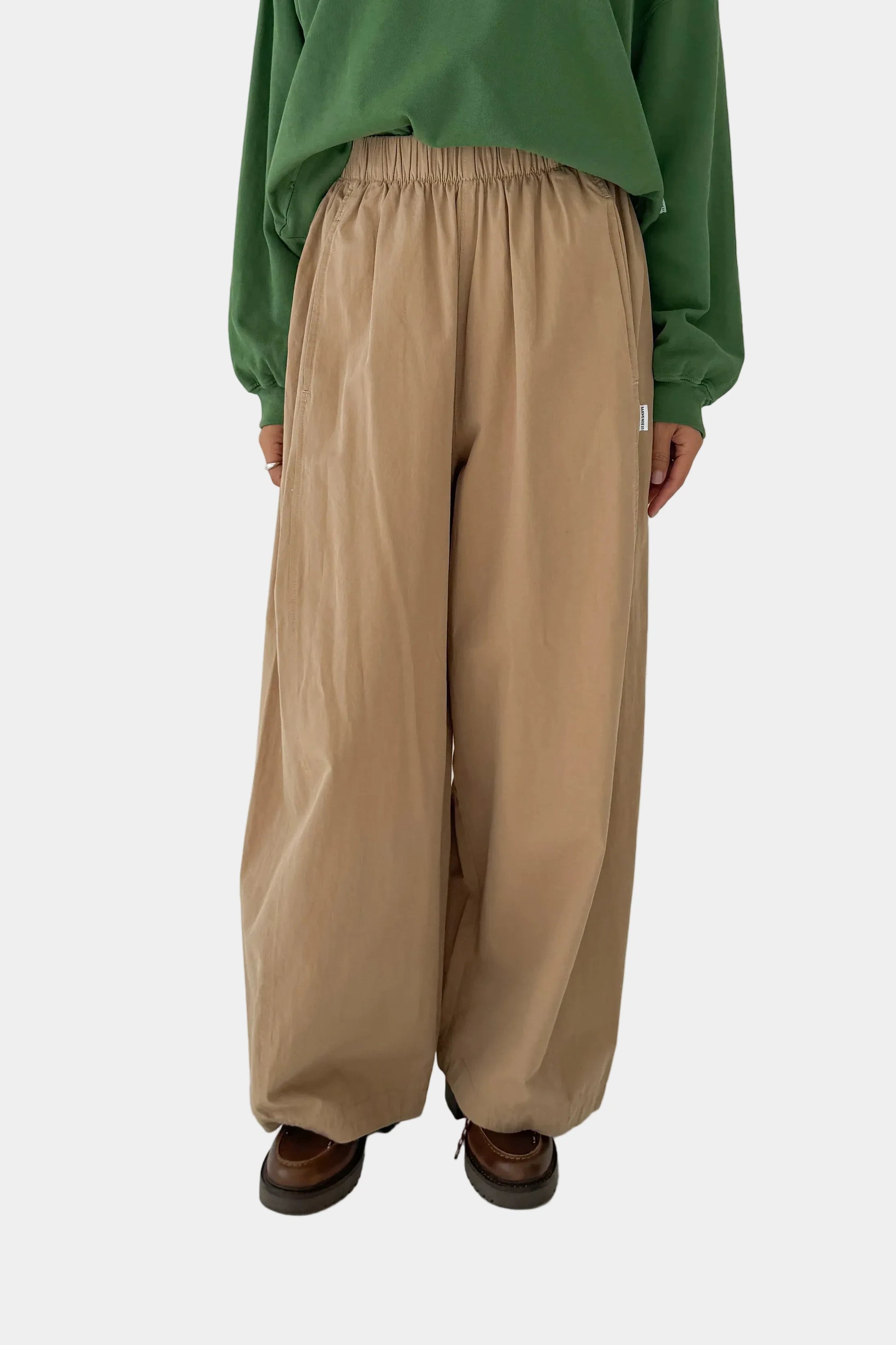 Person wearing beige wide-leg pants and a green top on a white background