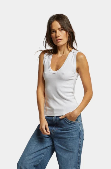 Woman wearing a white tank top and blue jeans against a plain background