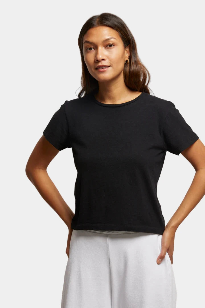 Woman wearing a black t-shirt and white pants against a neutral background