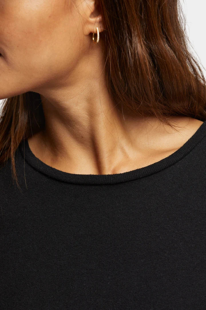 Close-up of a person wearing a black top and gold hoop earrings.