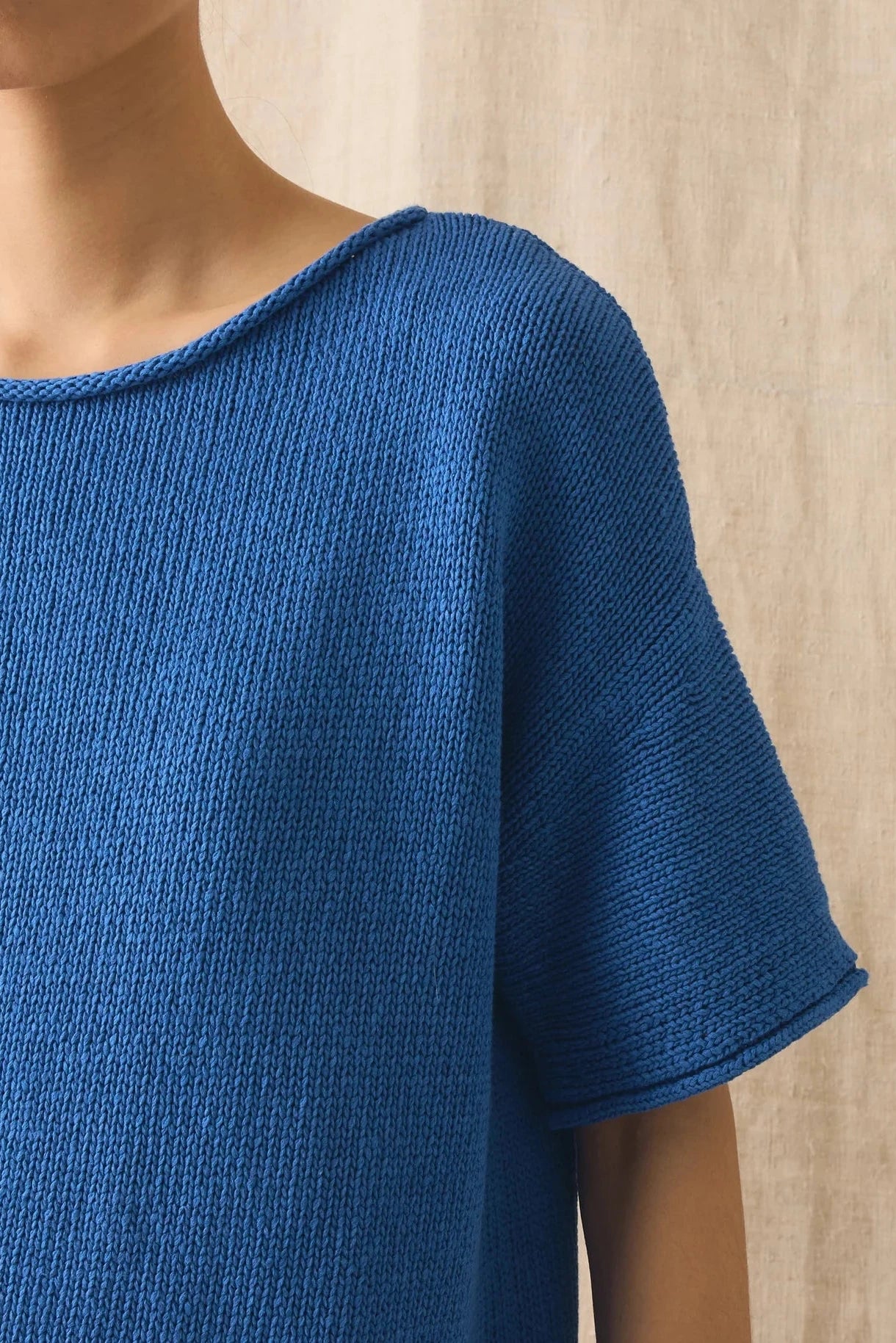 Blue knitted top worn by a person against a beige background