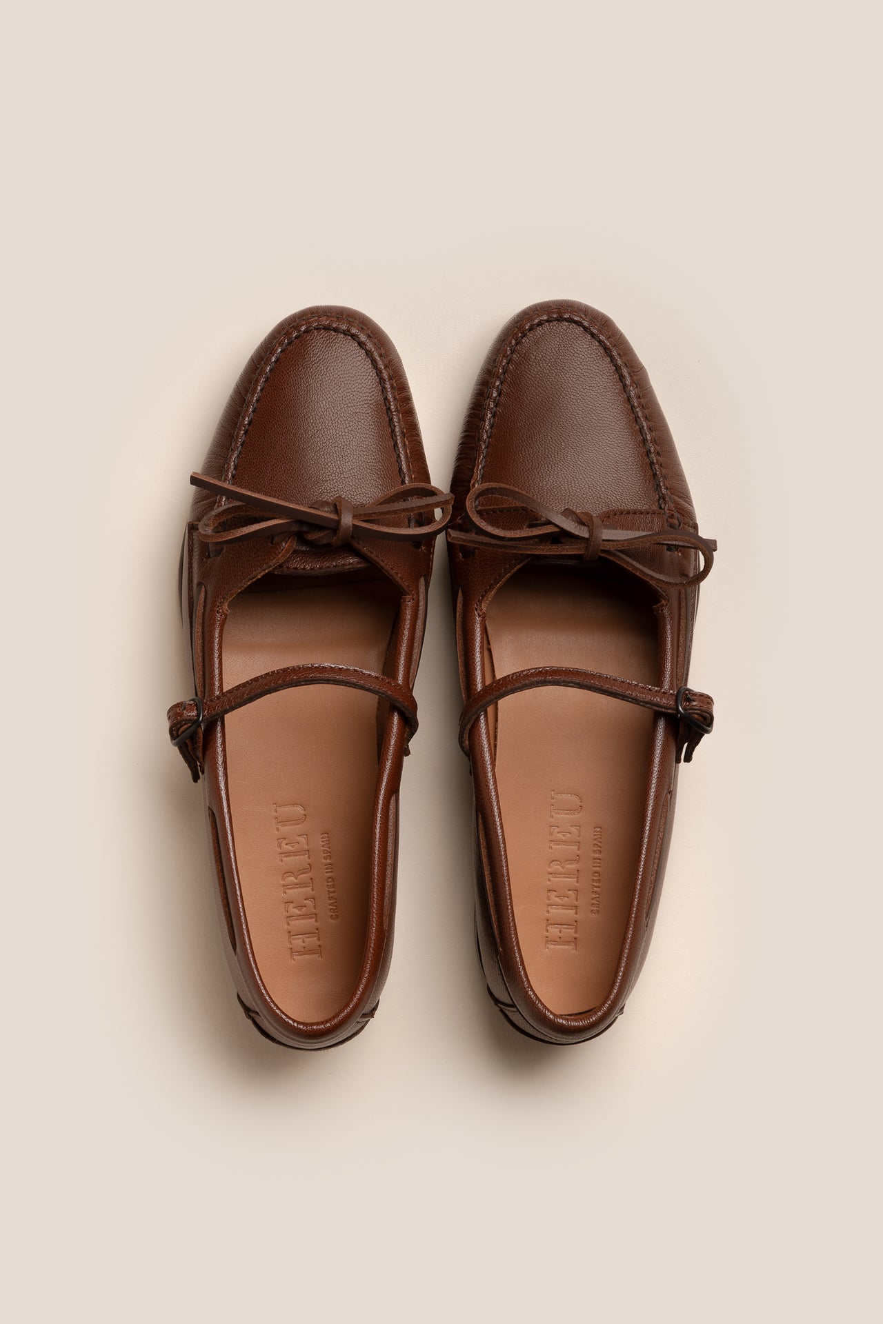 Pair of brown loafers with a brand logo on a beige background