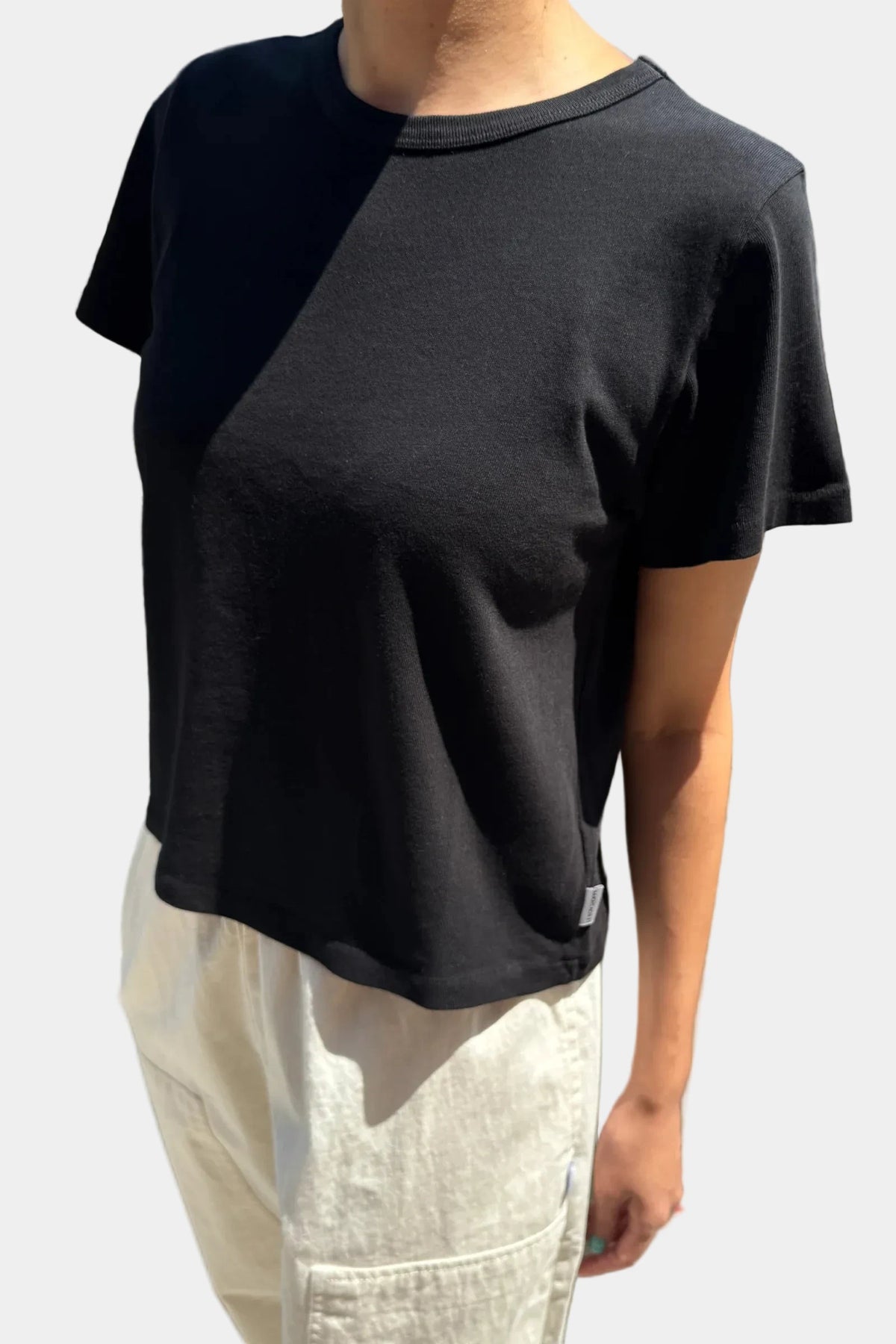 Side angle view of model wearing Le Bon Shoppe Little Boy Tee in True Black with light cream trousers