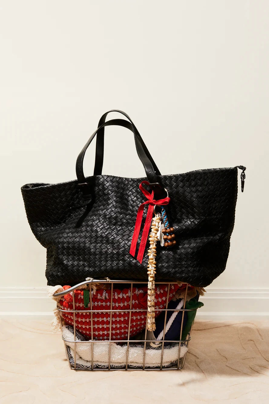 Black woven handbag with a red ribbon on a wire basket against a white background