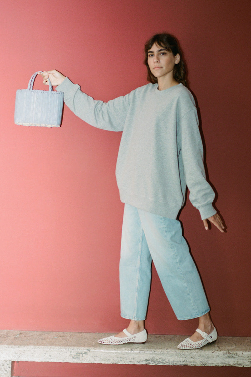 Woman in light blue outfit holding a basket against a pink wall