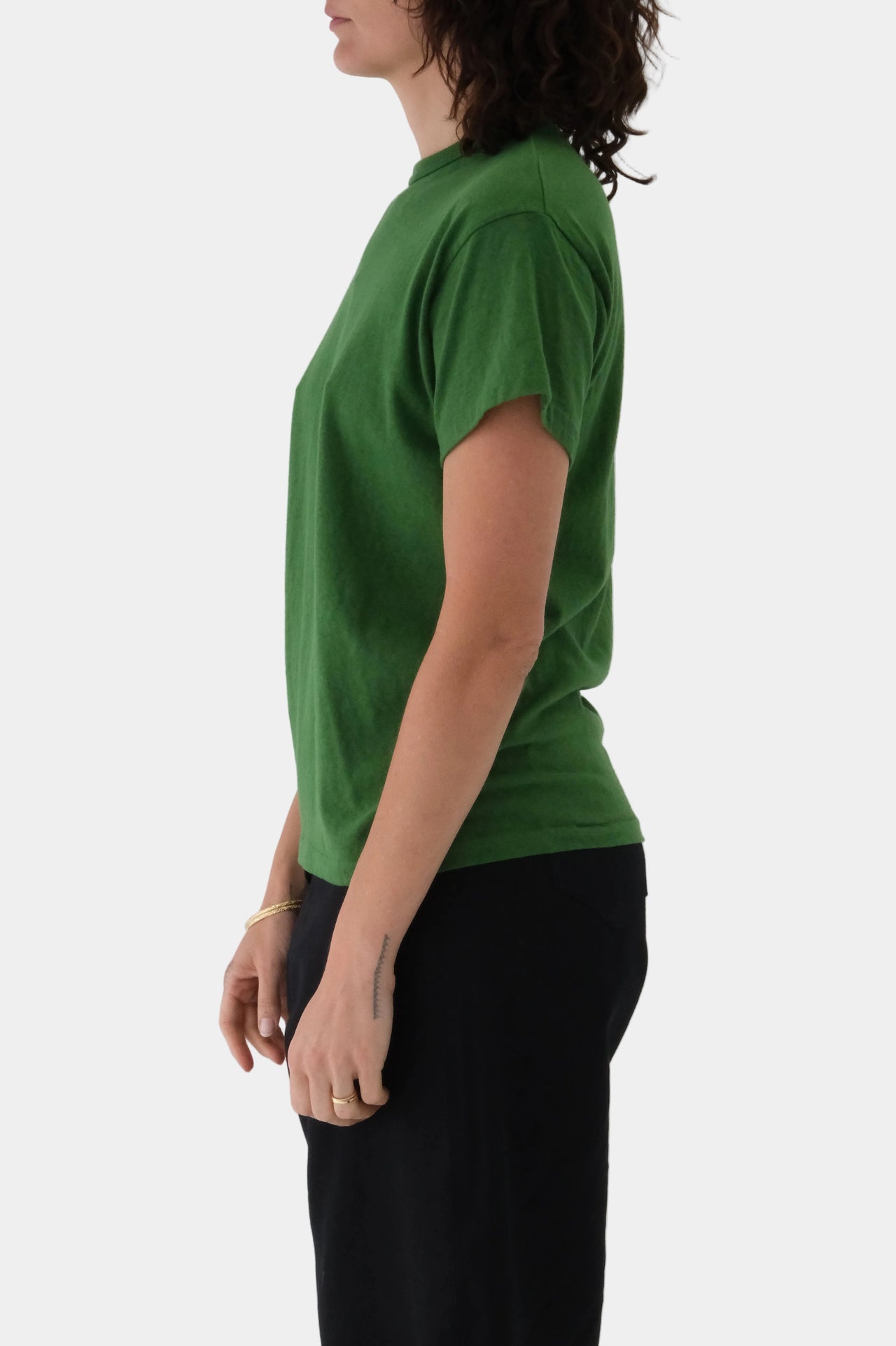 Person wearing a green t-shirt and black pants on a light gray background