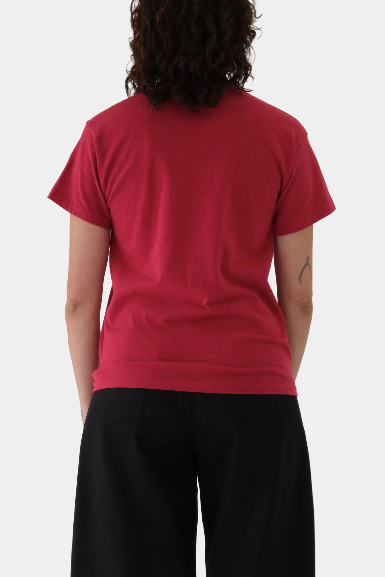 Person wearing a red t-shirt and black pants on a plain background