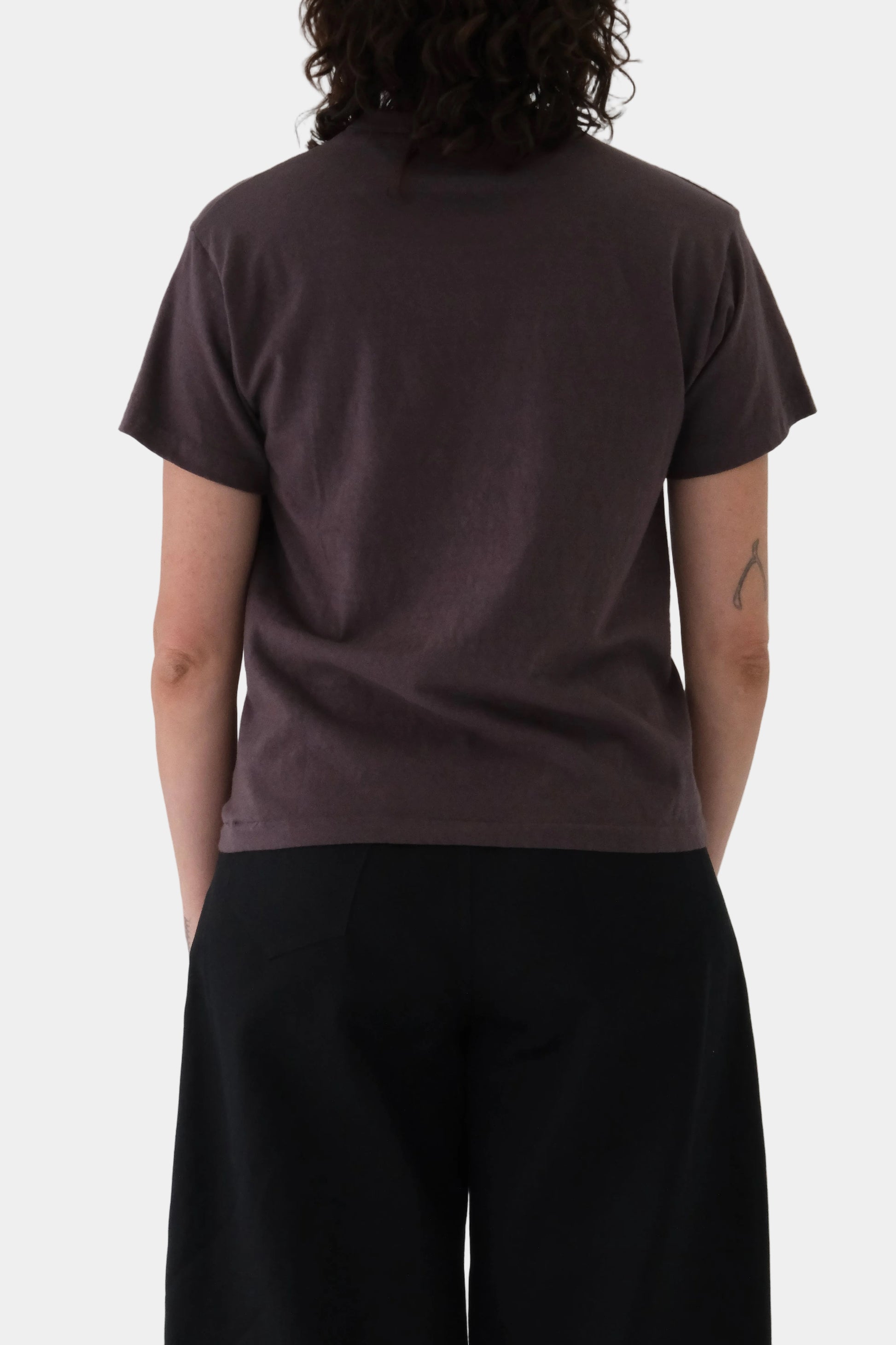 Person wearing a brown t-shirt and black pants against a light gray background