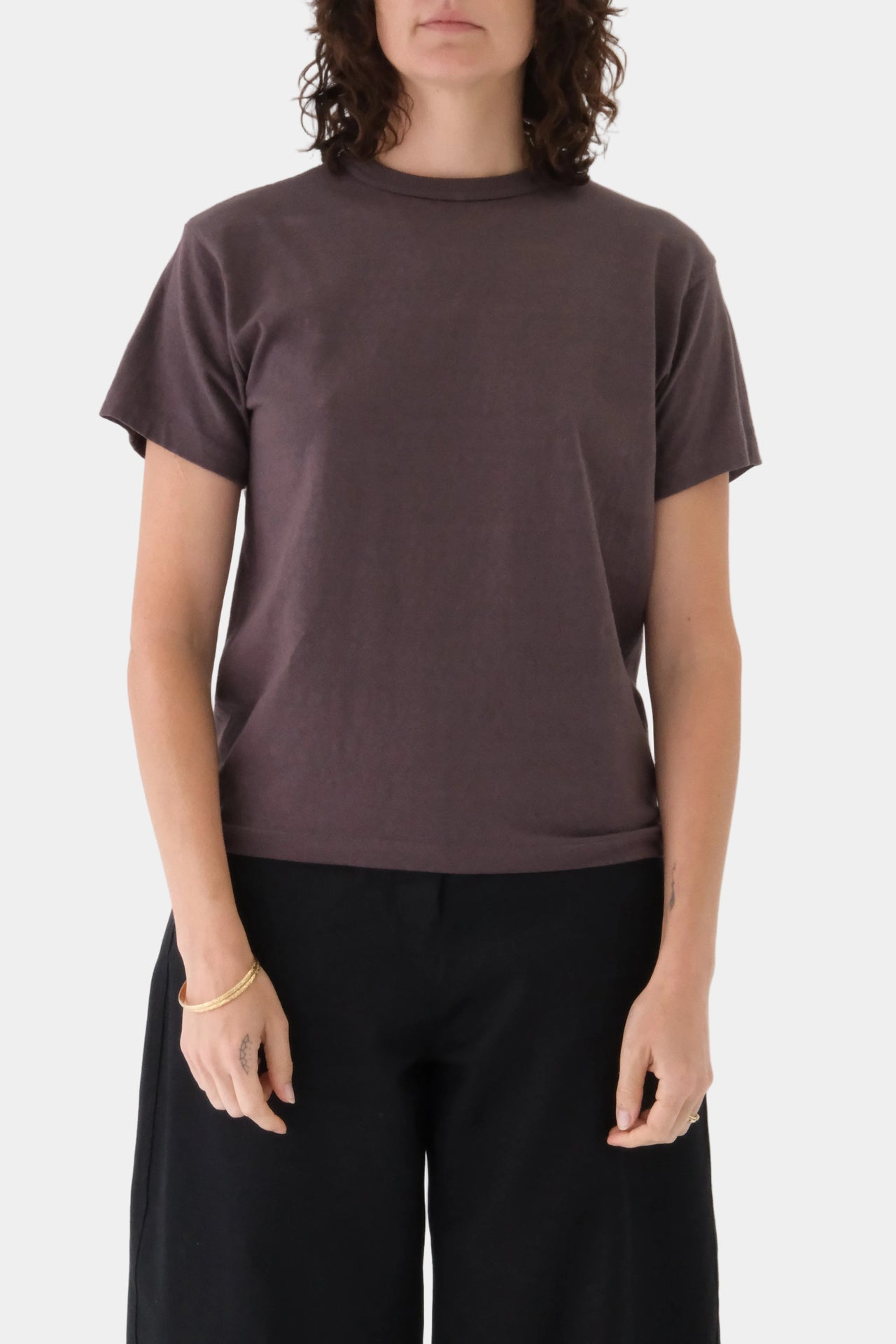 Person wearing a plain brown t-shirt and black pants on a white background