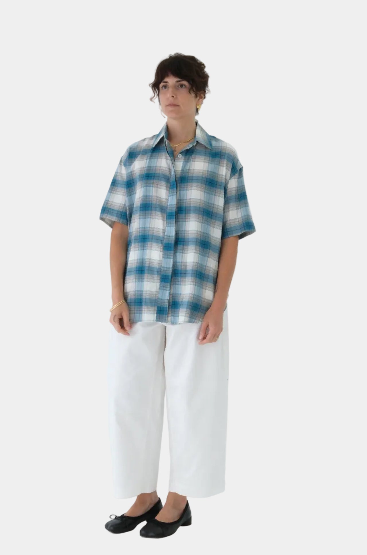 Person wearing a blue and white checkered shirt with white pants on a light gray background