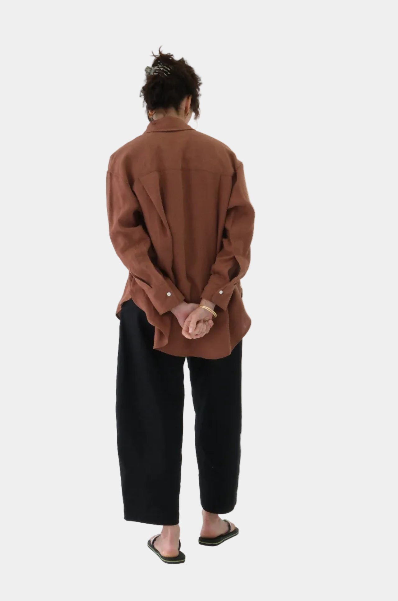 Person wearing a brown shirt and black pants on a white background