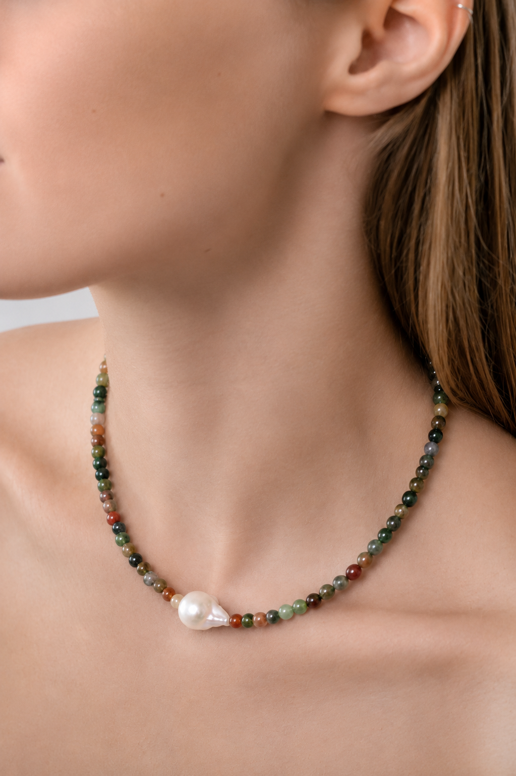 Necklace with multicolored beads and a pearl on a person's neck