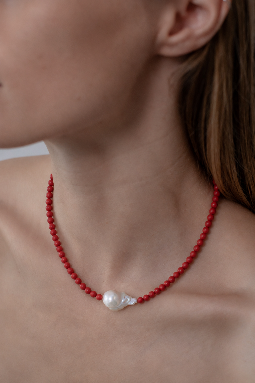 close up of a persons neck wearing a red coral necklace with central baroque pearl