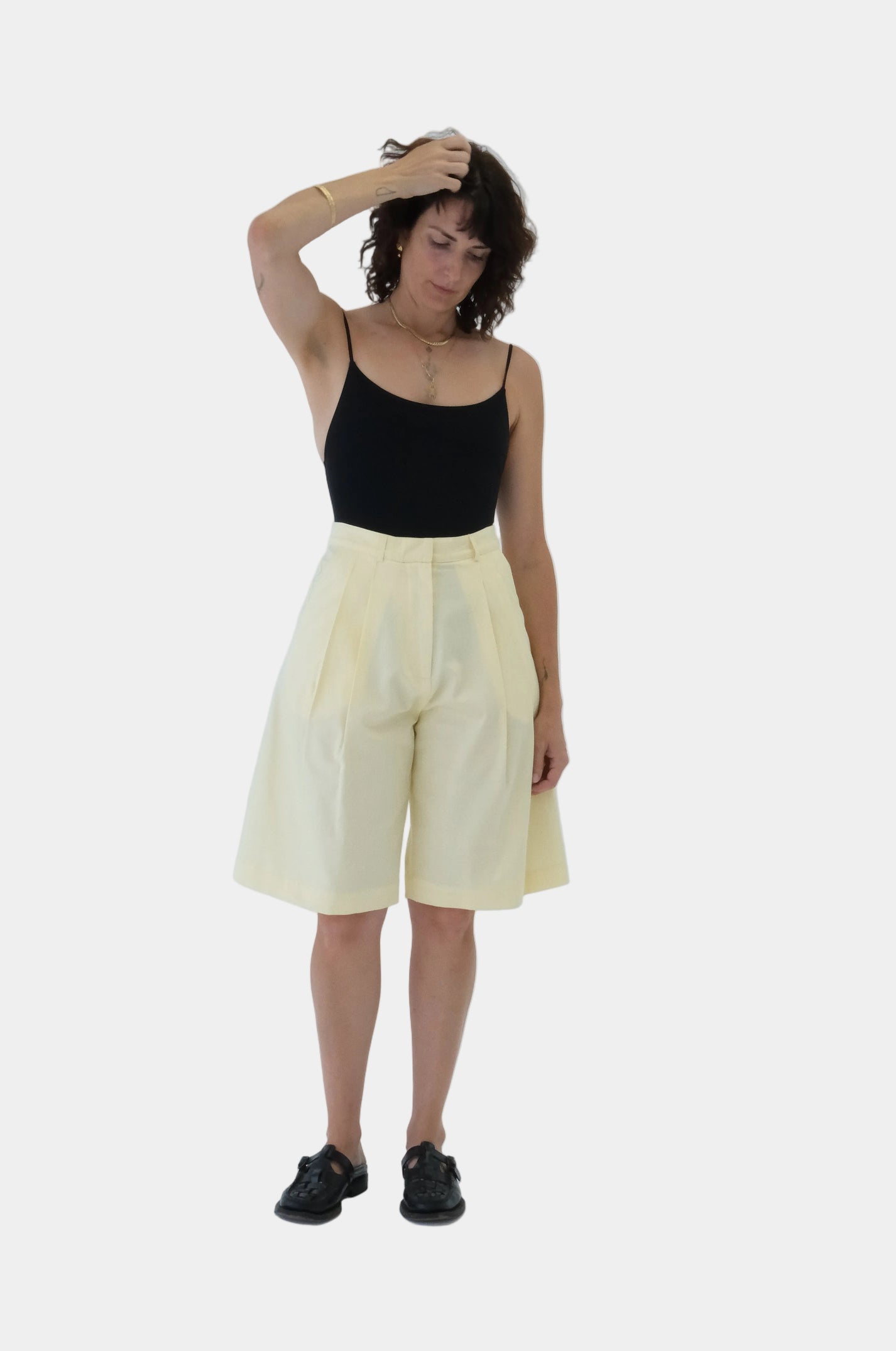 Person wearing a black top and butter yellow Bermuda tailored shorts on a light gray background