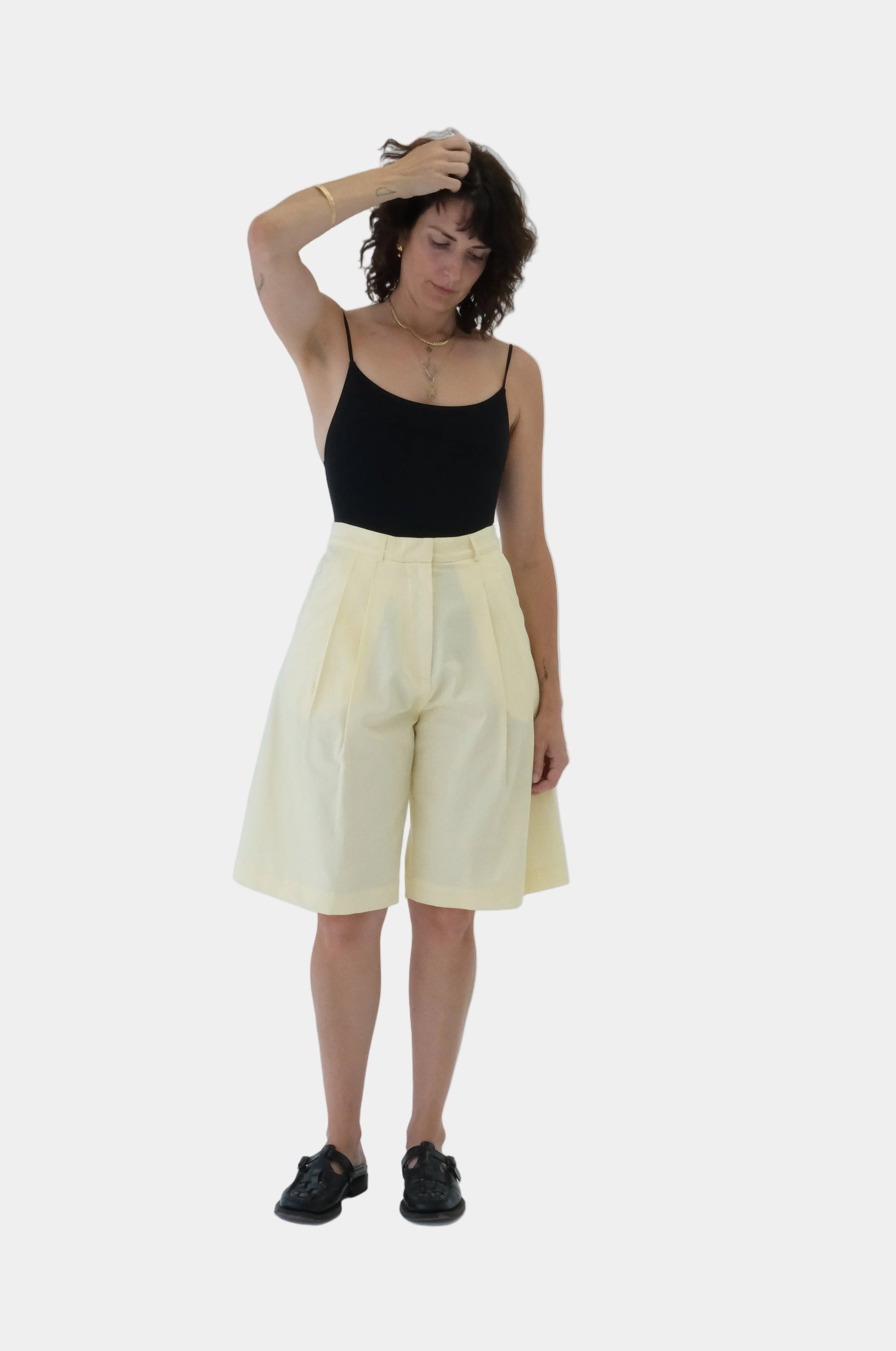 Person wearing a black top and butter yellow Bermuda tailored shorts on a light gray background