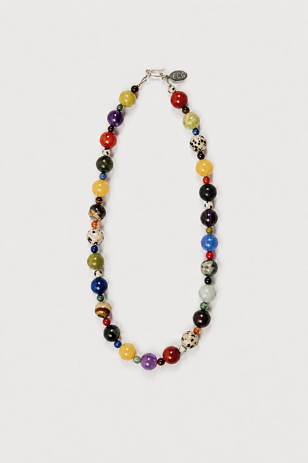 A colorful beaded necklace with a mix of solid, marbled, and patterned round beads in red, yellow, green, blue, purple, black, and white, arranged in an oval shape on a light gray background.