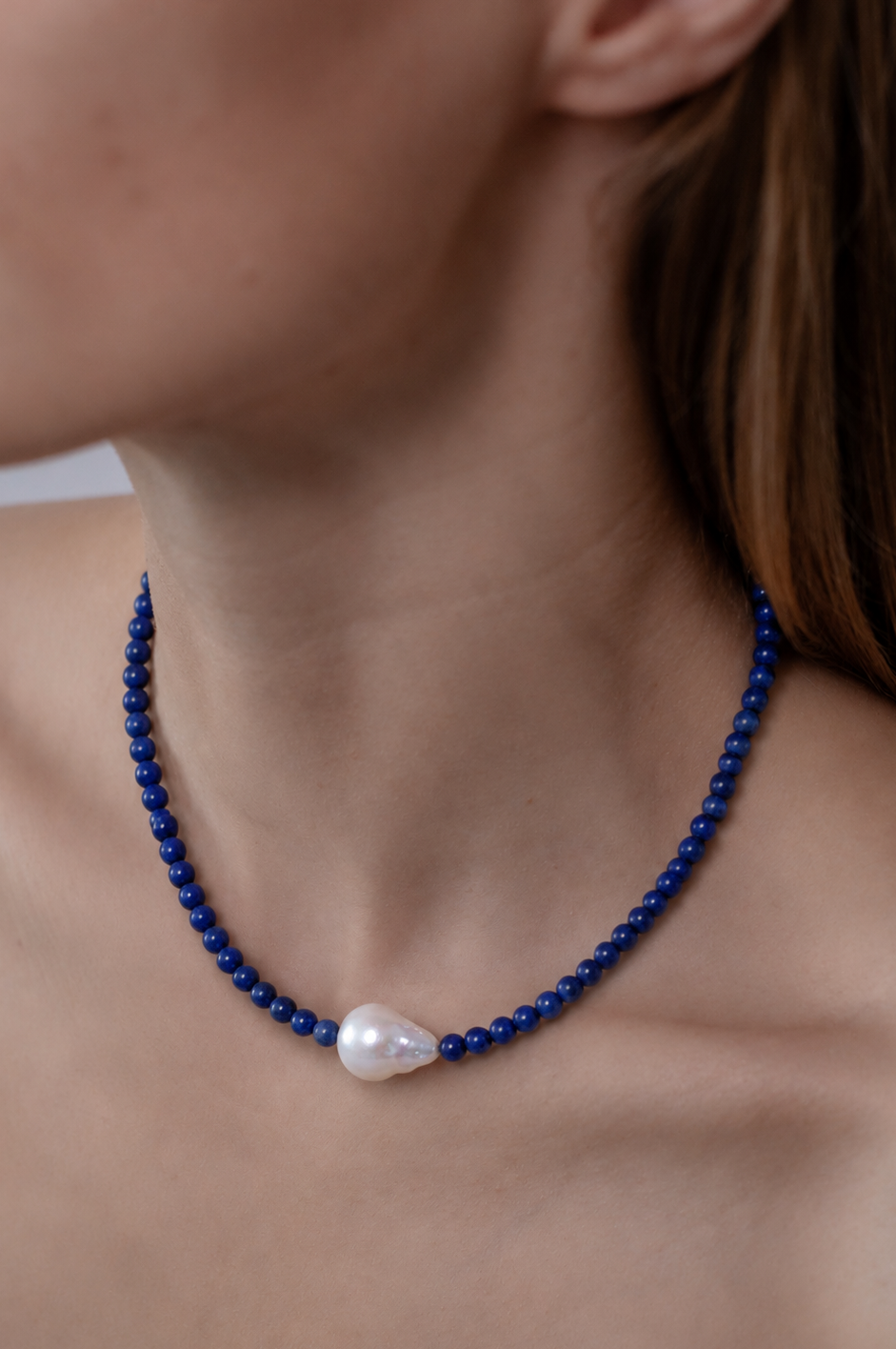 close up of a persons neck wearing a blue lapis beaded necklace with a central baroque pearl.
