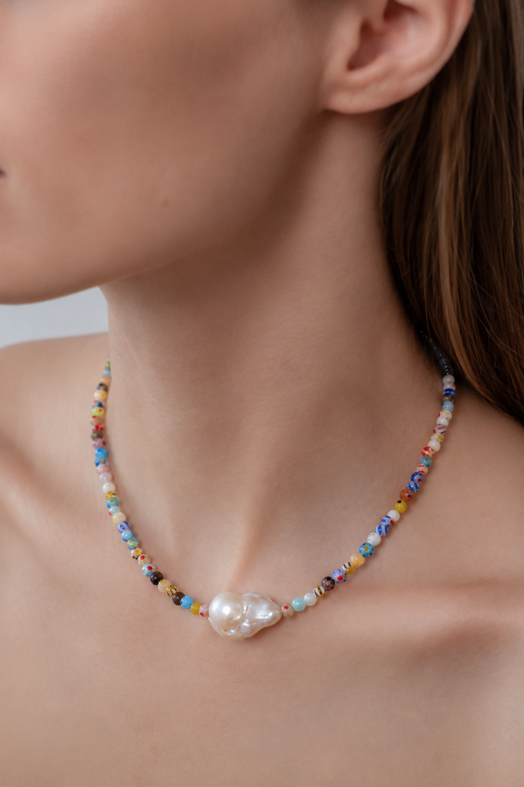 Close-up of a colorful beaded necklace with a pearl pendant on a person.