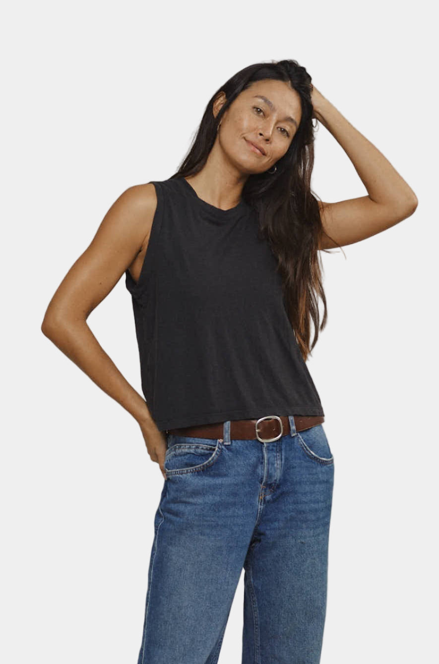 Woman wearing a black tank top and blue jeans on a plain background