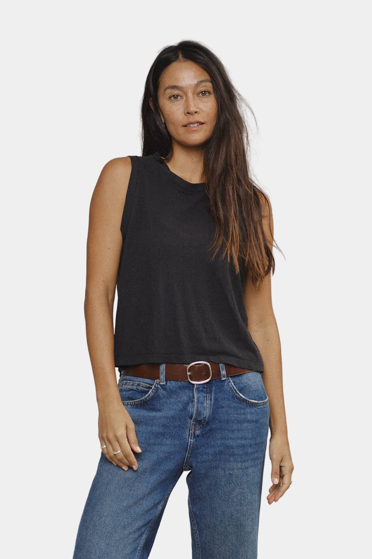 Woman wearing a black tank top and blue jeans on a plain background
