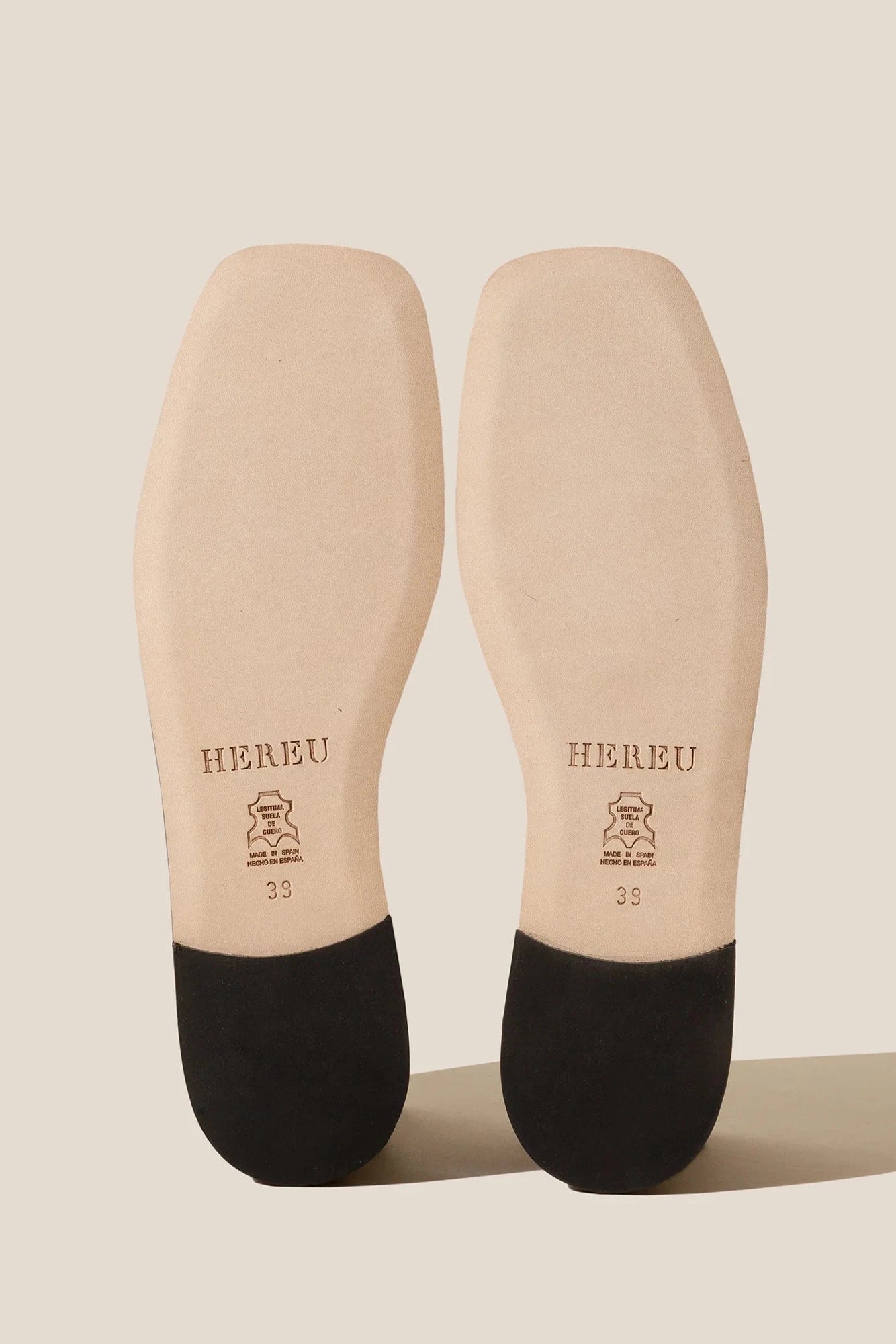 Beige insoles with black toes on a beige background, featuring the brand 'HEREU'.