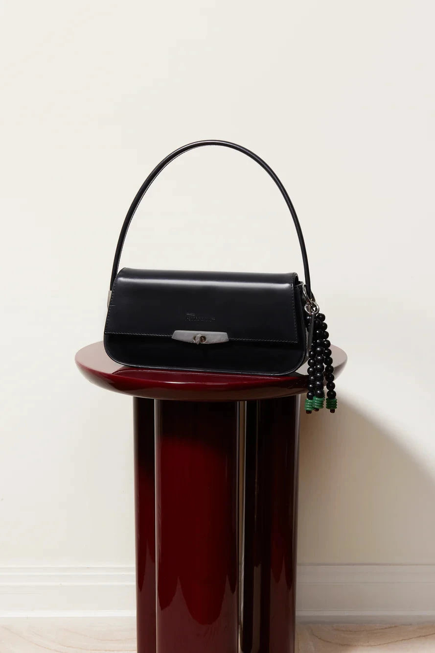 Black handbag with green accents on a red pedestal against a white background