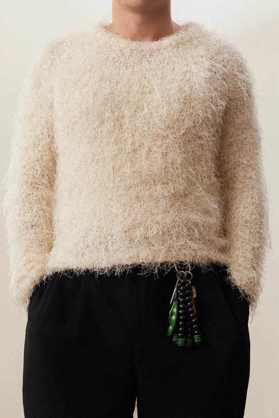 Person wearing a fluffy beige sweater and black pants with a neutral background