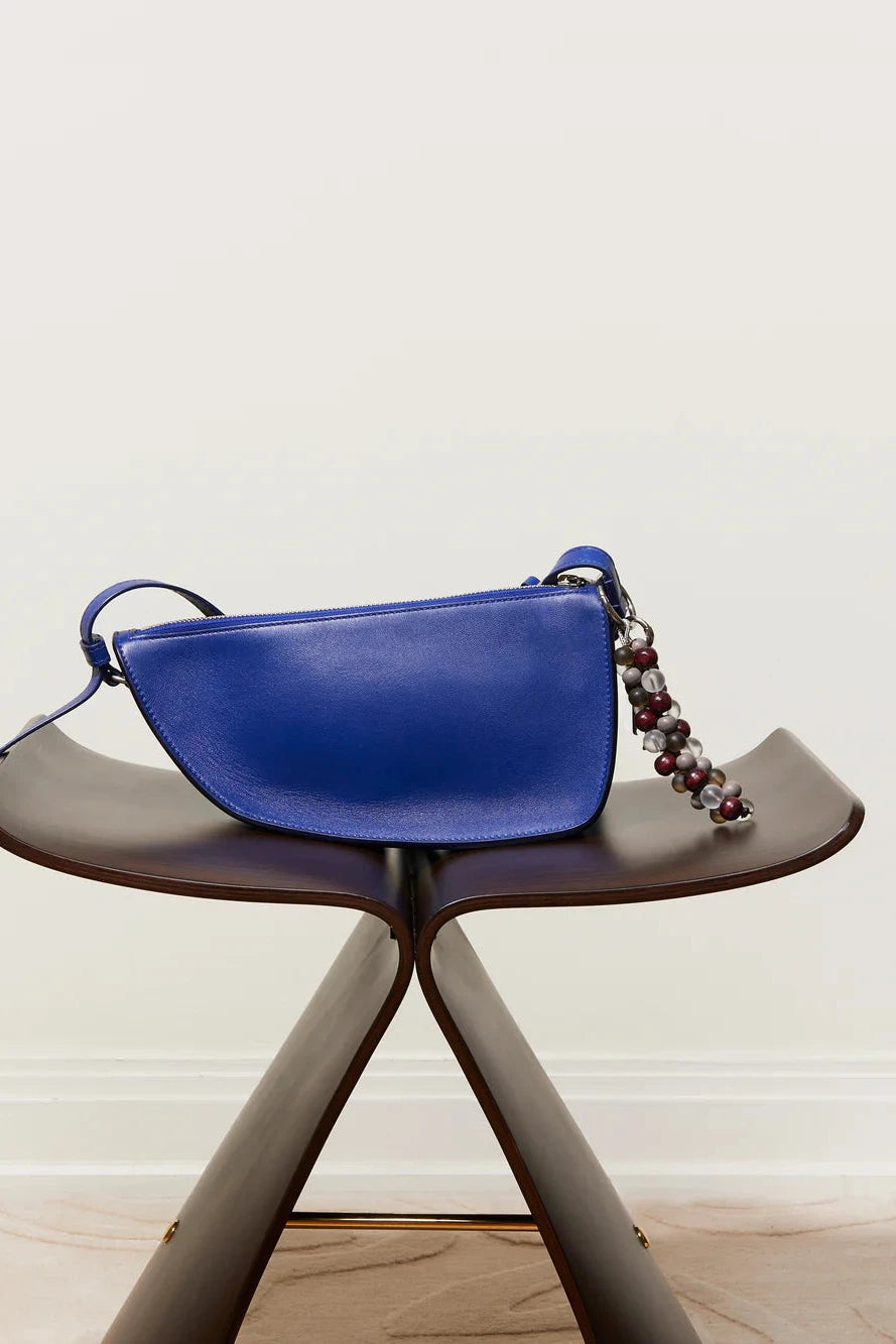Blue handbag with a chain detail on a wooden stool against a light background