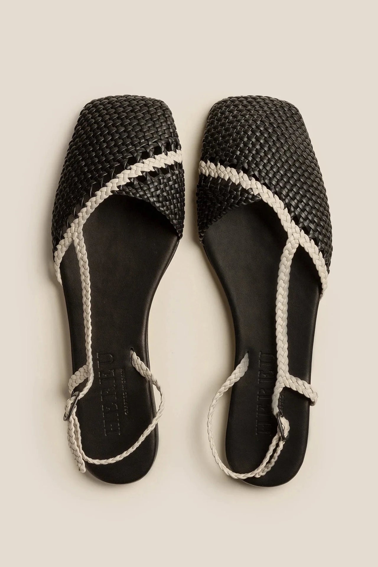 Pair of black woven sandals with white straps on a beige background