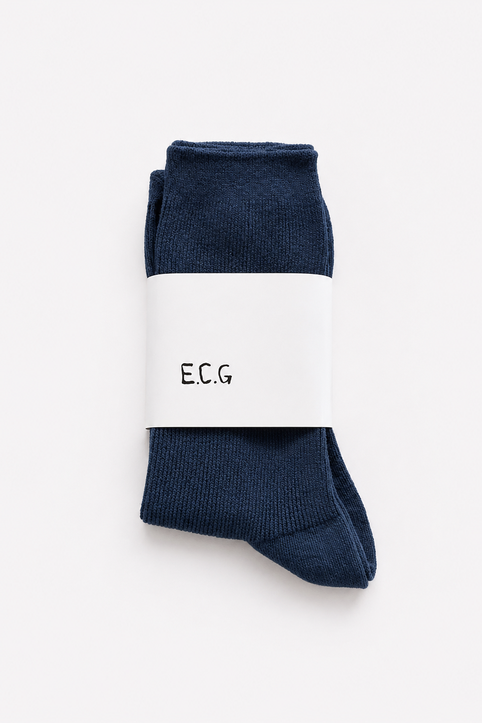 A pair of petrol blue cotton ribbed crew socks folded and wrapped in a white paper band with the letters 'E.C.G’ - East Coast General