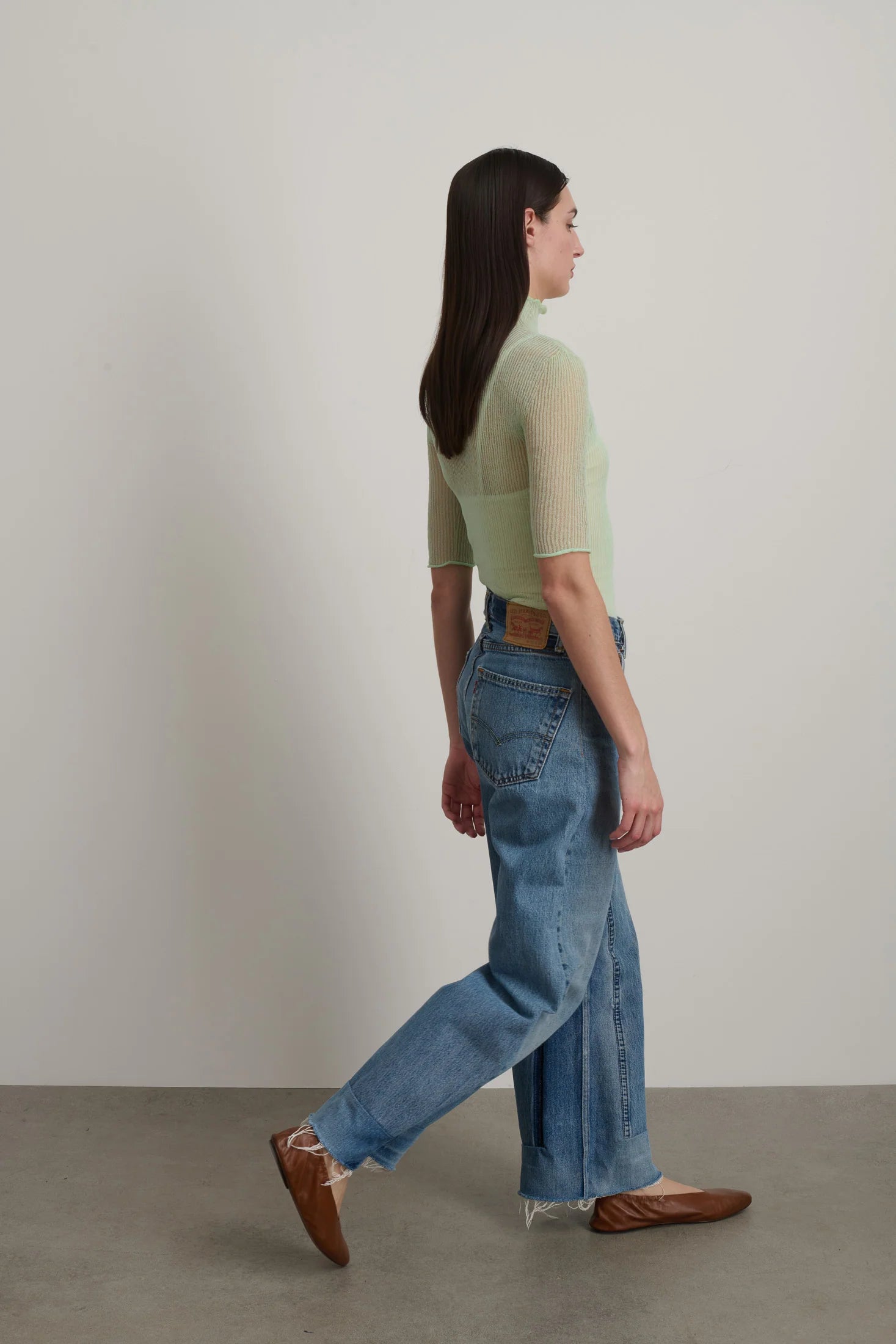 Woman wearing a green top and blue jeans walking on a plain background