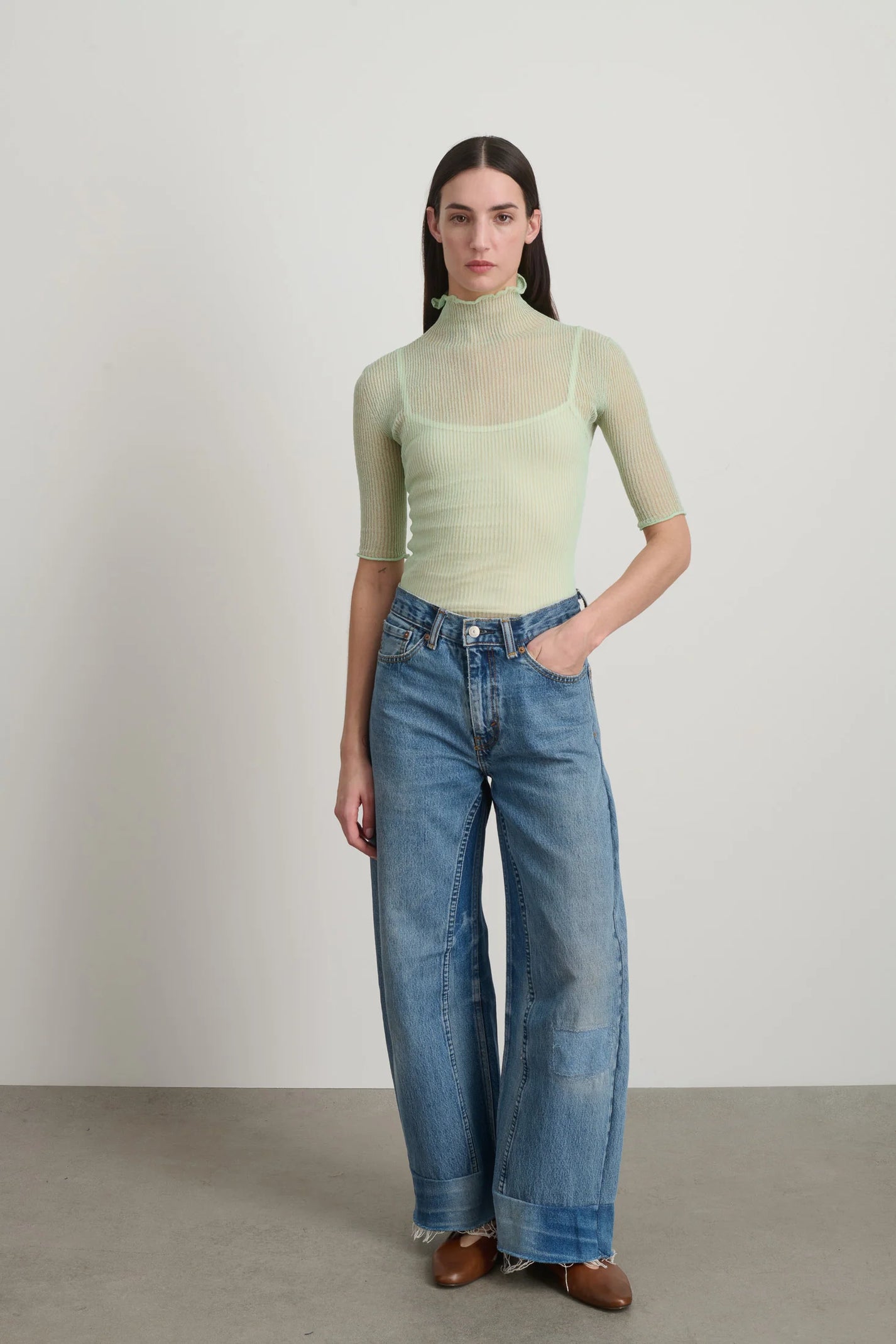 Woman wearing a light green top and blue jeans against a plain background