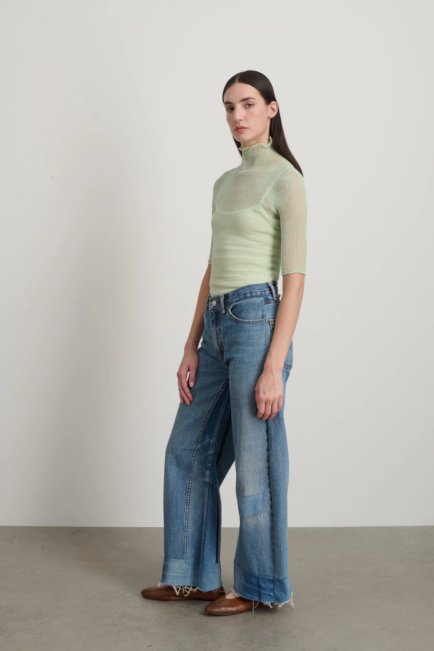 Woman wearing a light green turtleneck and blue jeans against a plain background