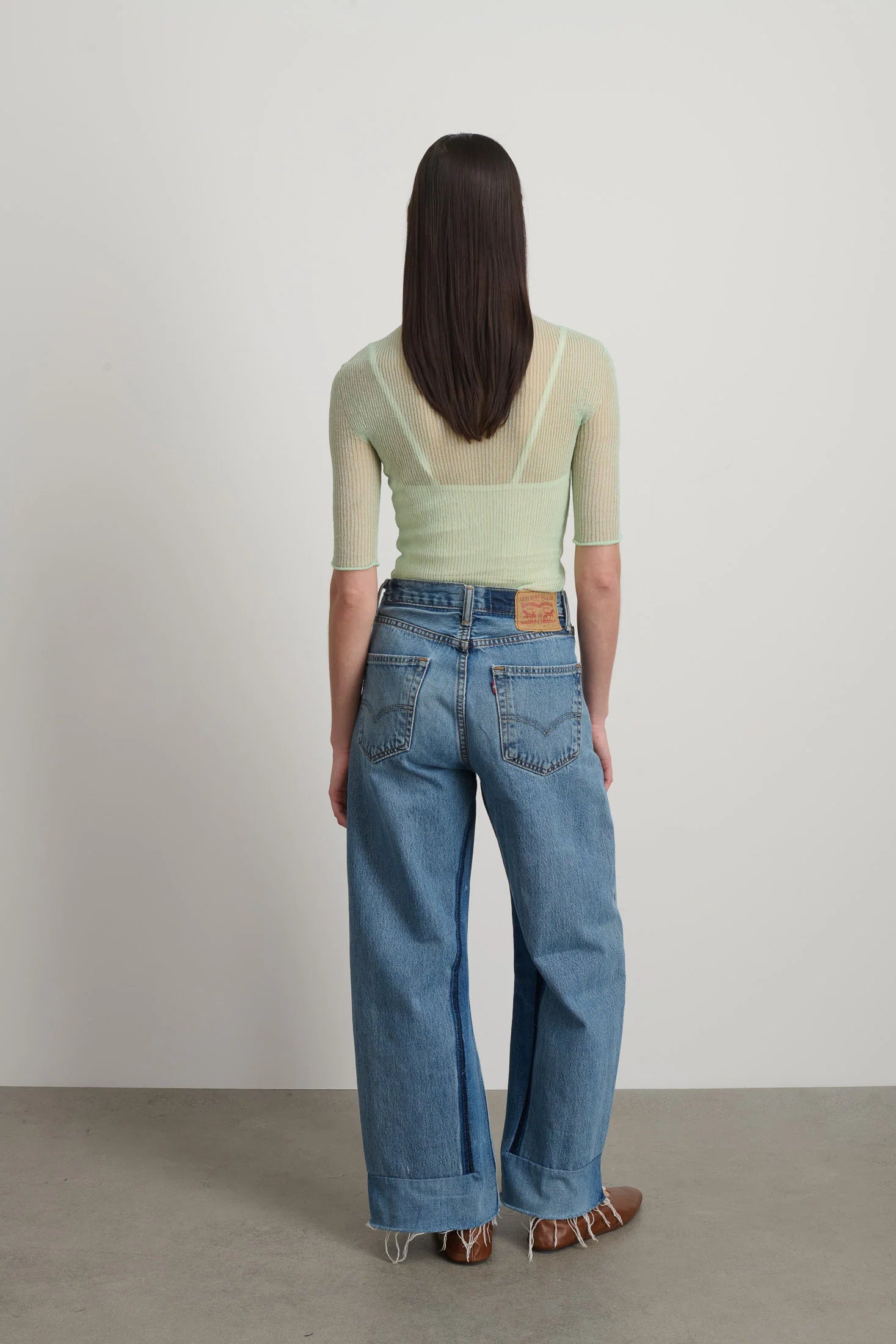 Person wearing a light green top and blue jeans with a visible brand logo on a plain background