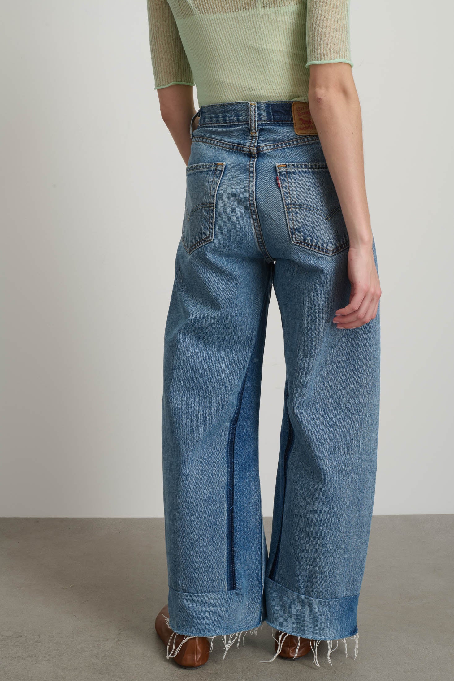 Person wearing blue wide-leg jeans and a light green top against a neutral background