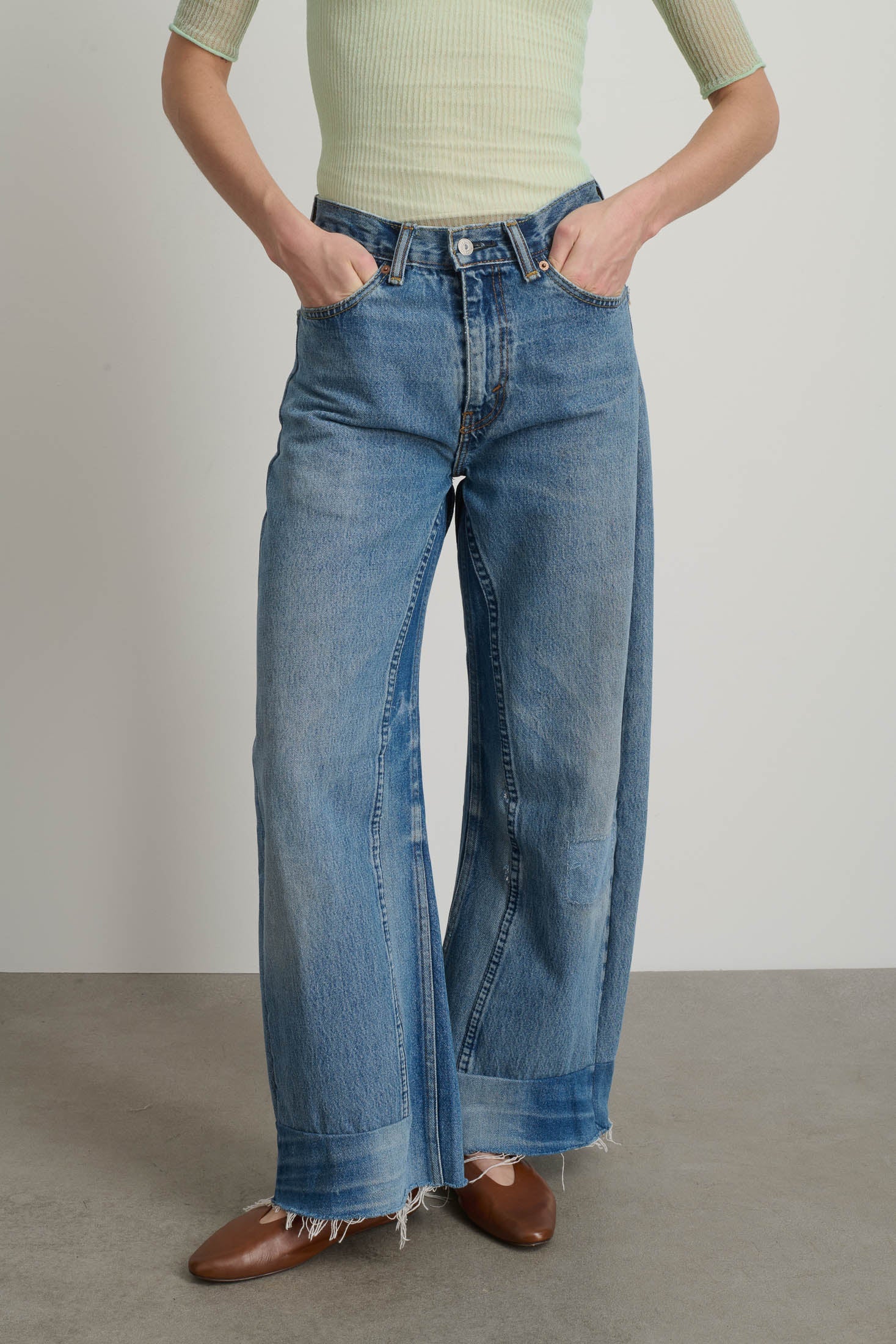 Person wearing blue jeans and a light green top against a plain background