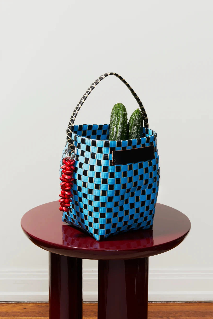 Blue checkered bag with red tassels on a wooden stool against a white wall
