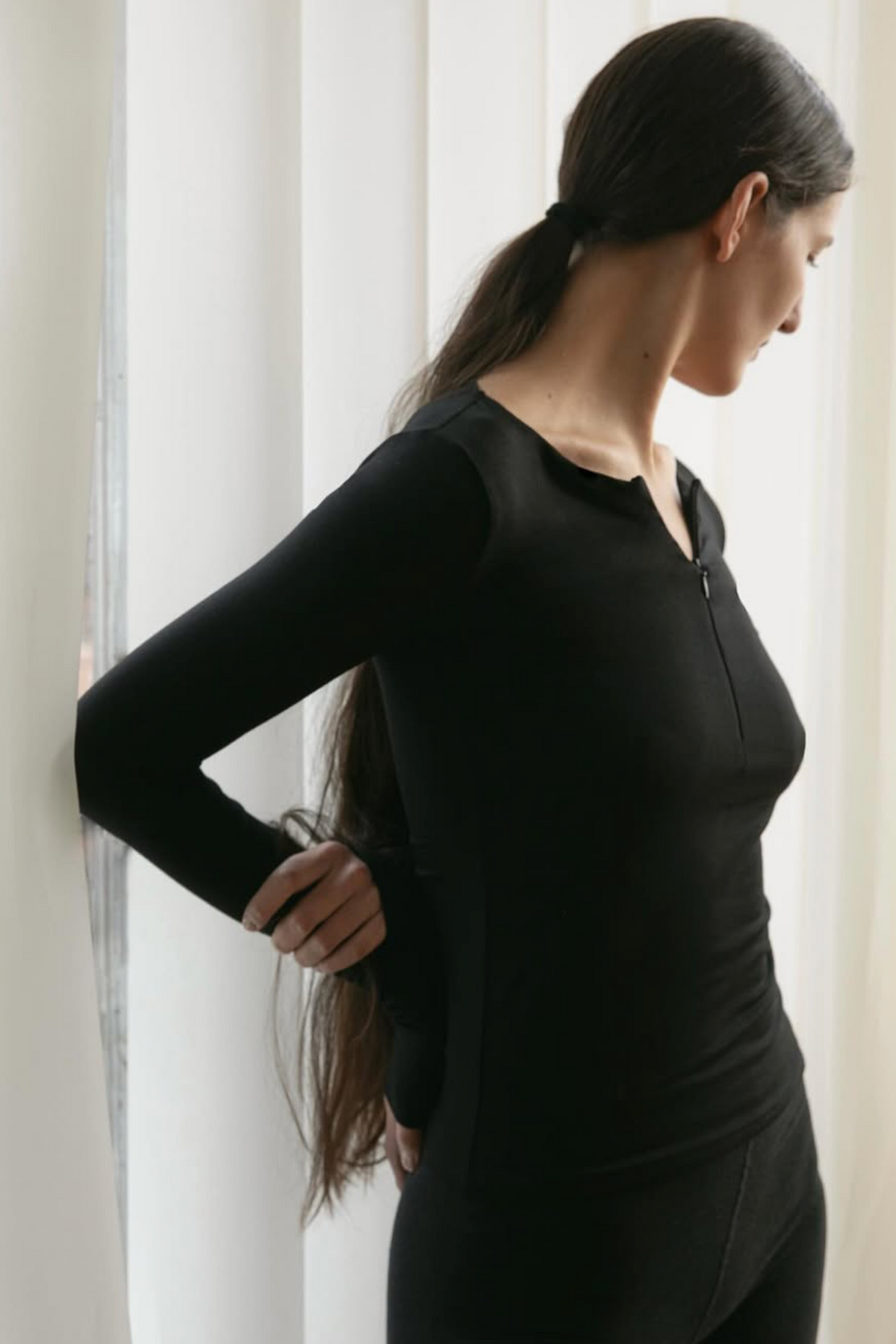 A women wearing the Kye Intimates Half Zip in black, standing in front of a curtain - East Coast General