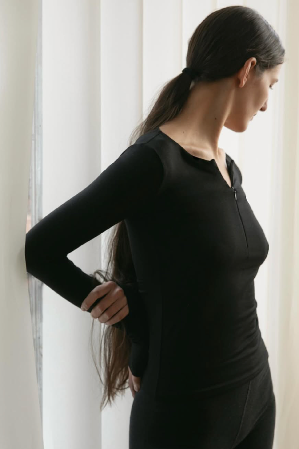 A women wearing the Kye Intimates Half Zip in black, standing in front of a curtain - East Coast General