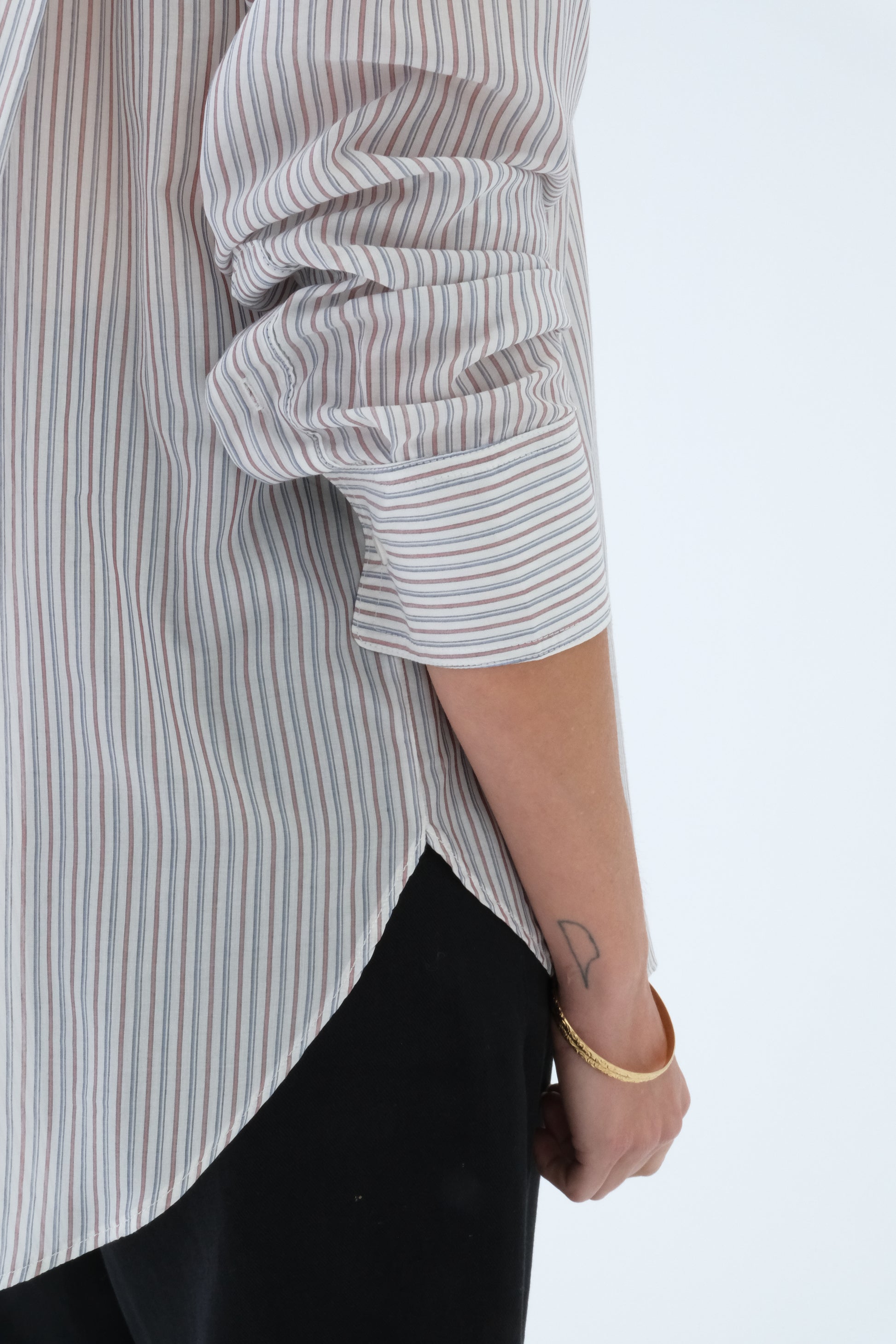 Person wearing a striped shirt with rolled-up sleeves on a light gray background