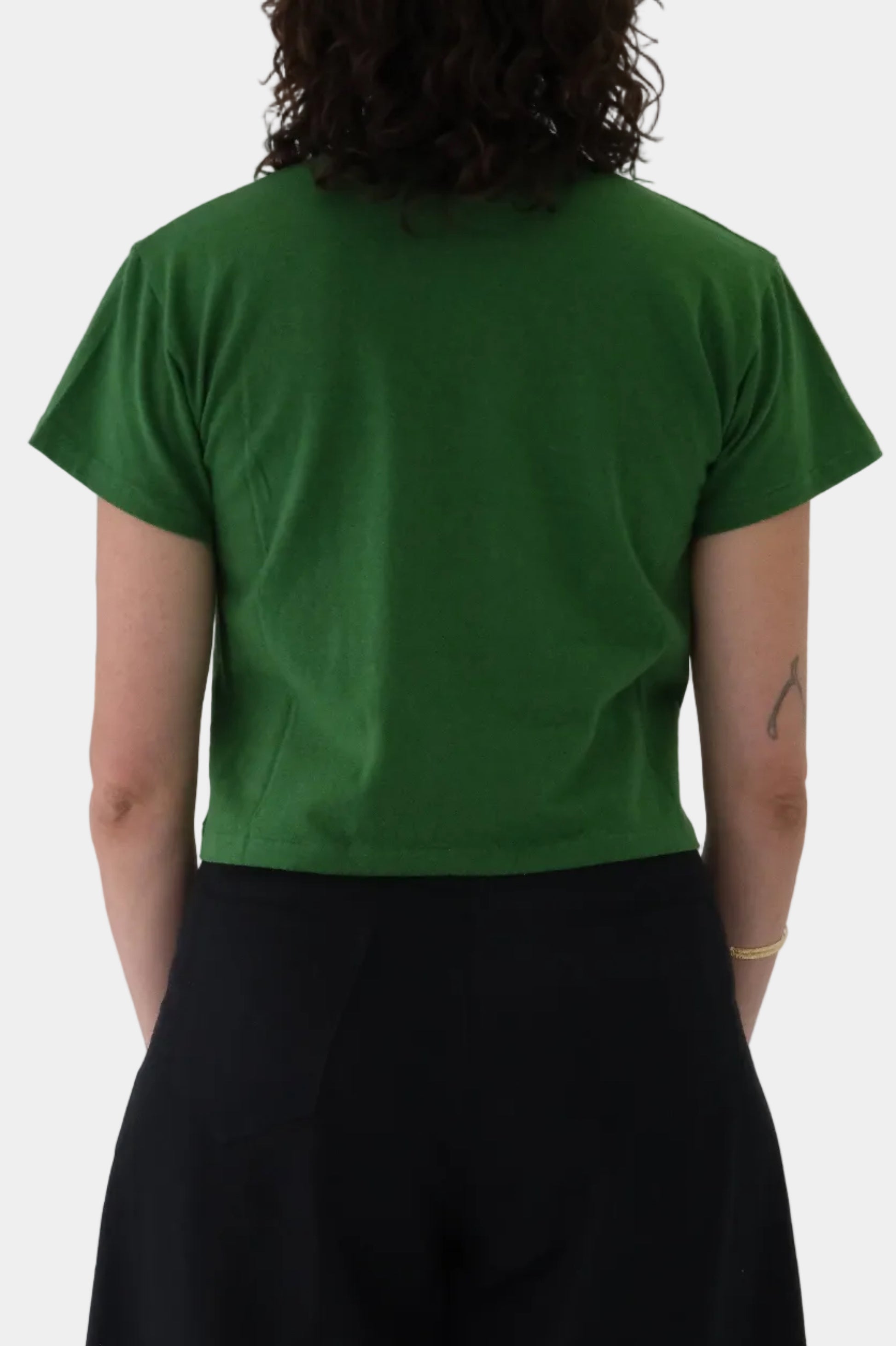 Person wearing a green t-shirt and black pants against a light gray background