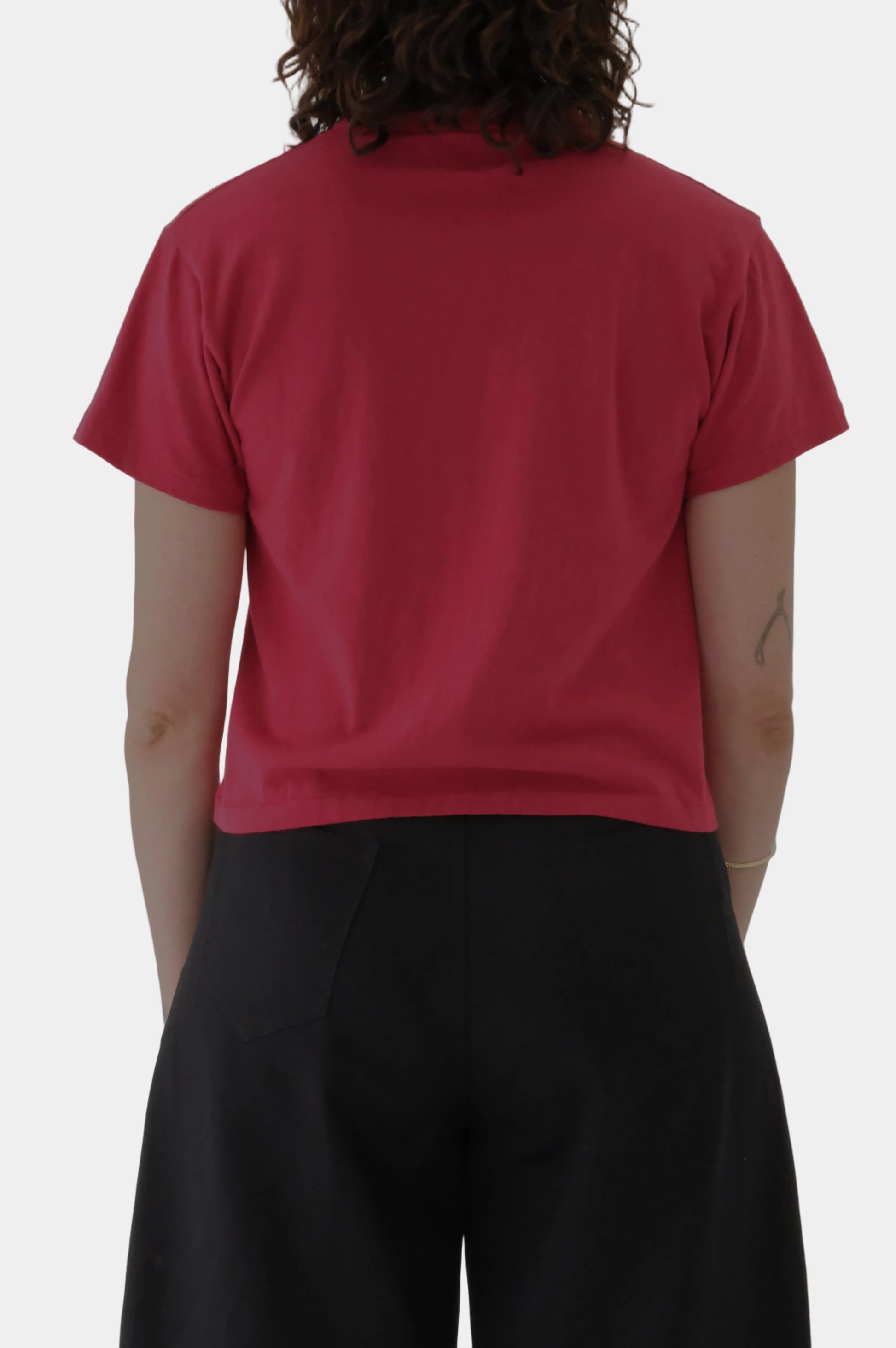 Person wearing a red t-shirt and black pants on a plain background