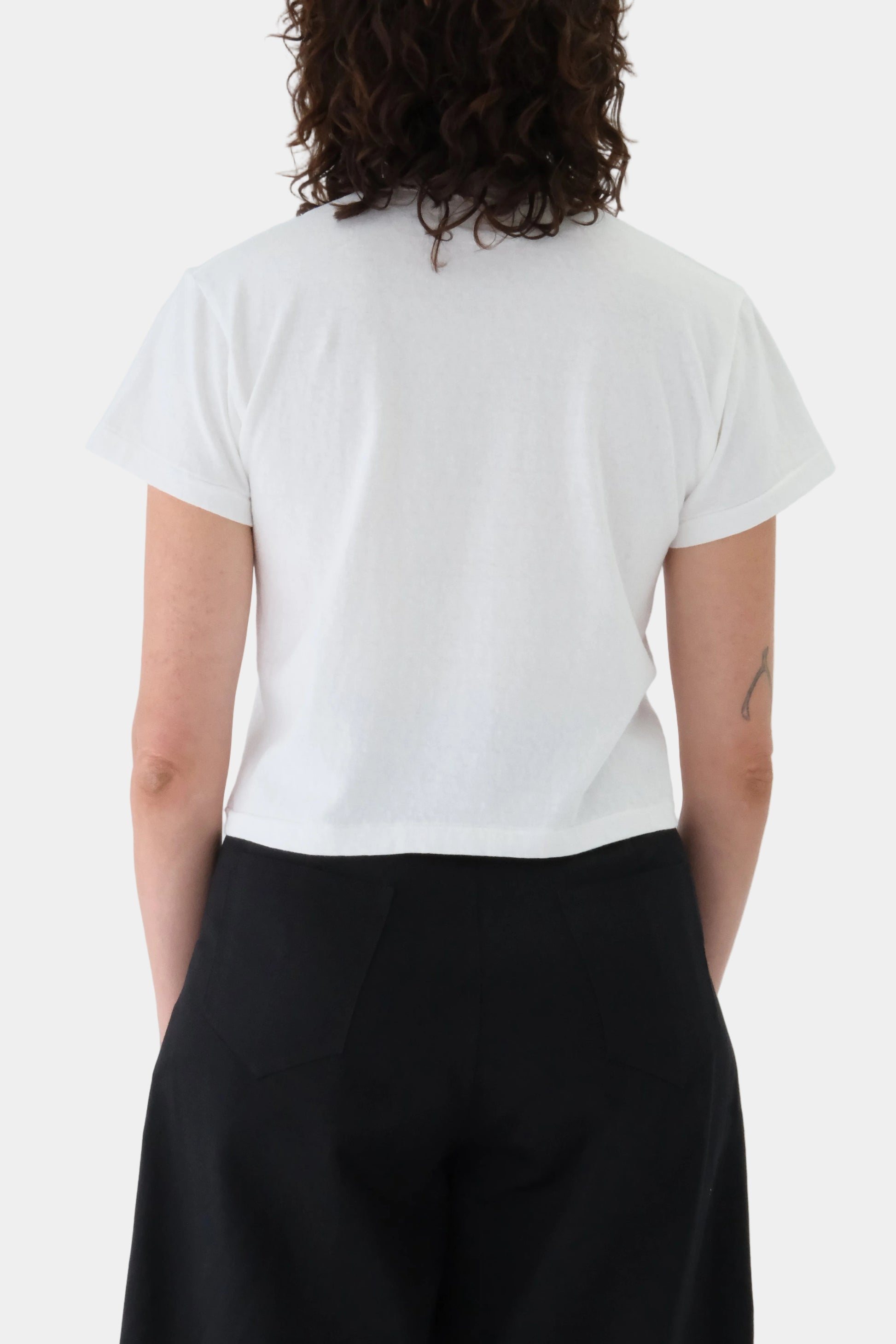 Person wearing a white t-shirt and black pants against a plain background