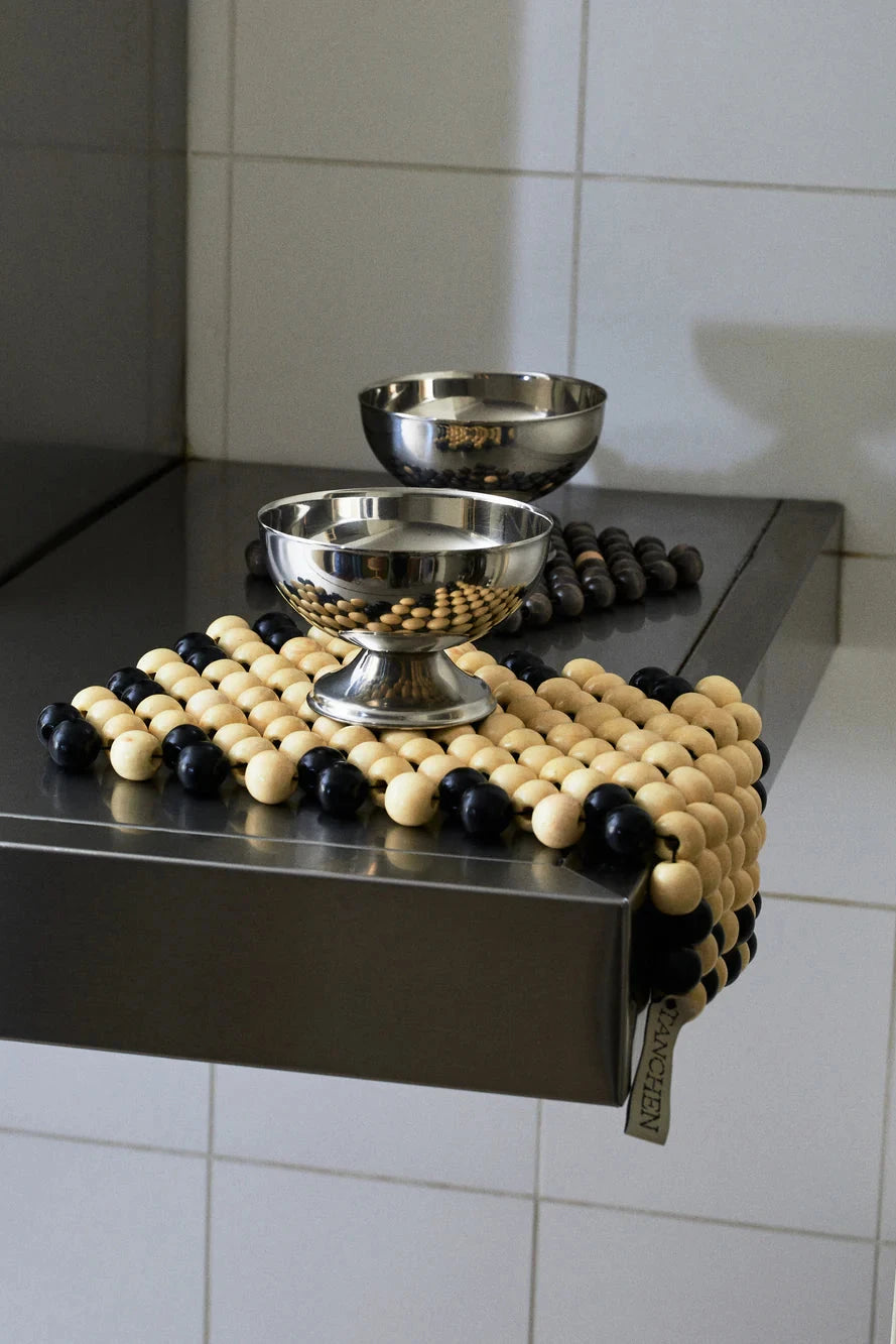 Decorative tray with black and beige beads on a metallic surface against a tiled wall.