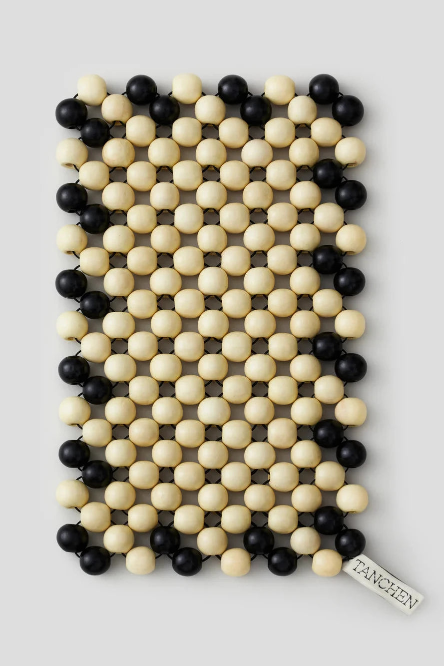 Decorative tray with black and beige beads on a metallic surface against a tiled wall.