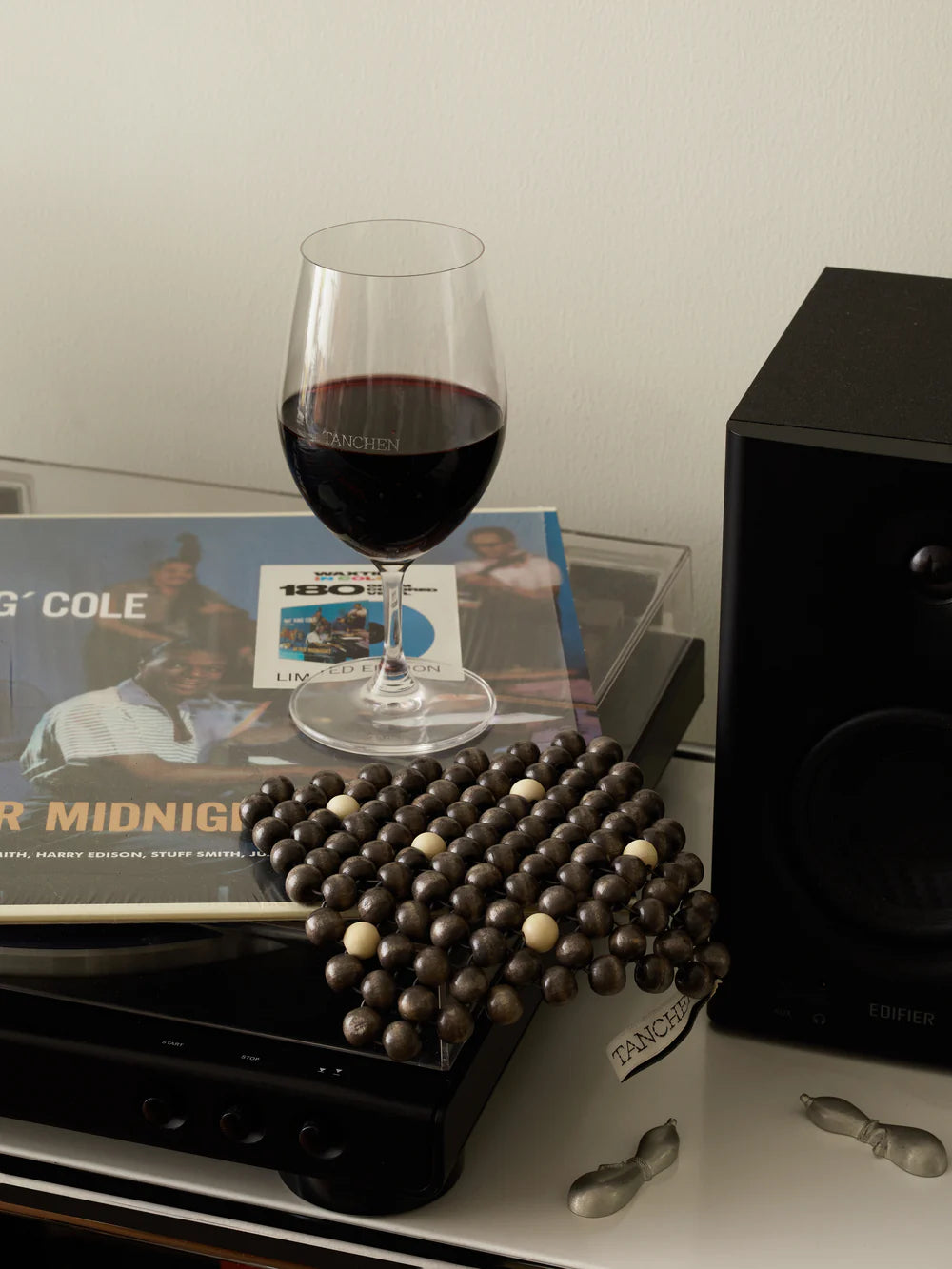 Wine glass with red wine on a record player with a record and a speaker in the background.