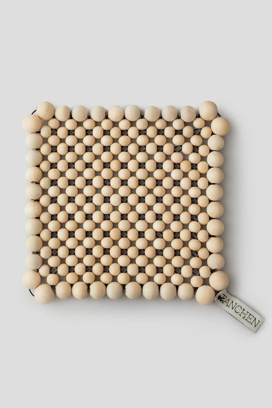 Beaded trivet with a brand tag on a light gray background
