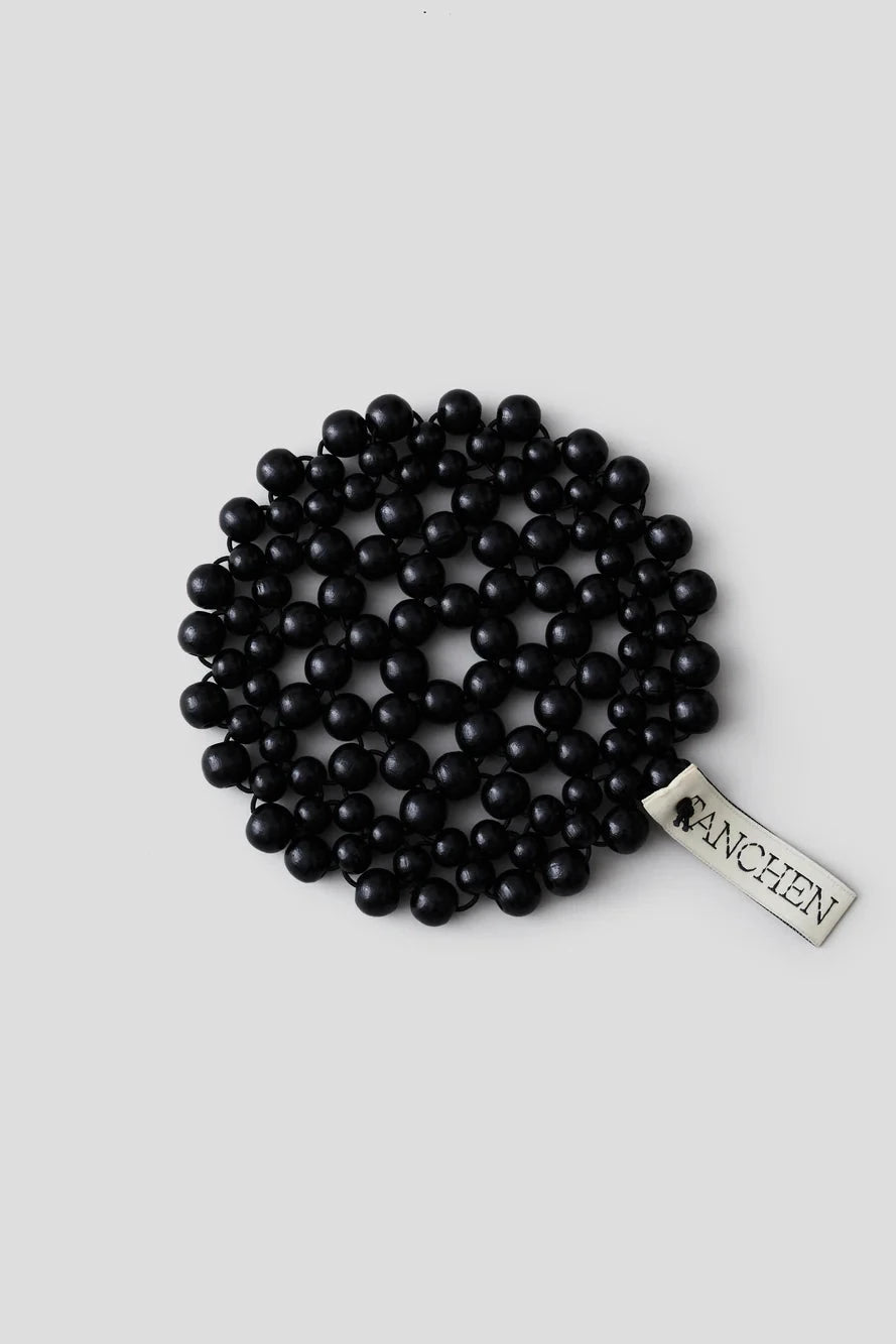 Black beaded bracelet with a visible brand label on a light gray background