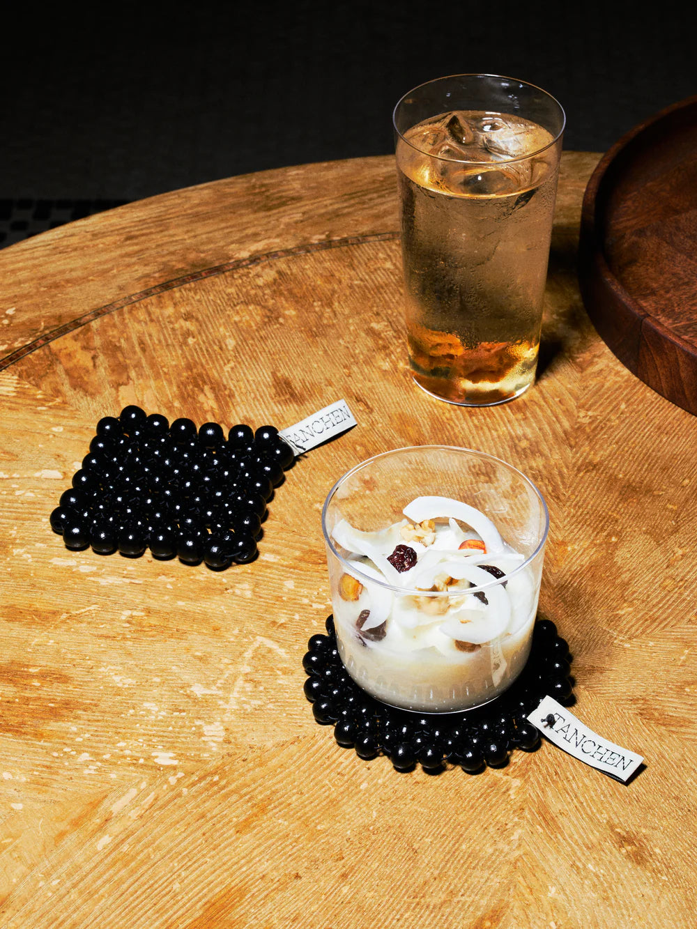 Two glasses of drinks on a wooden surface with black bead coasters.