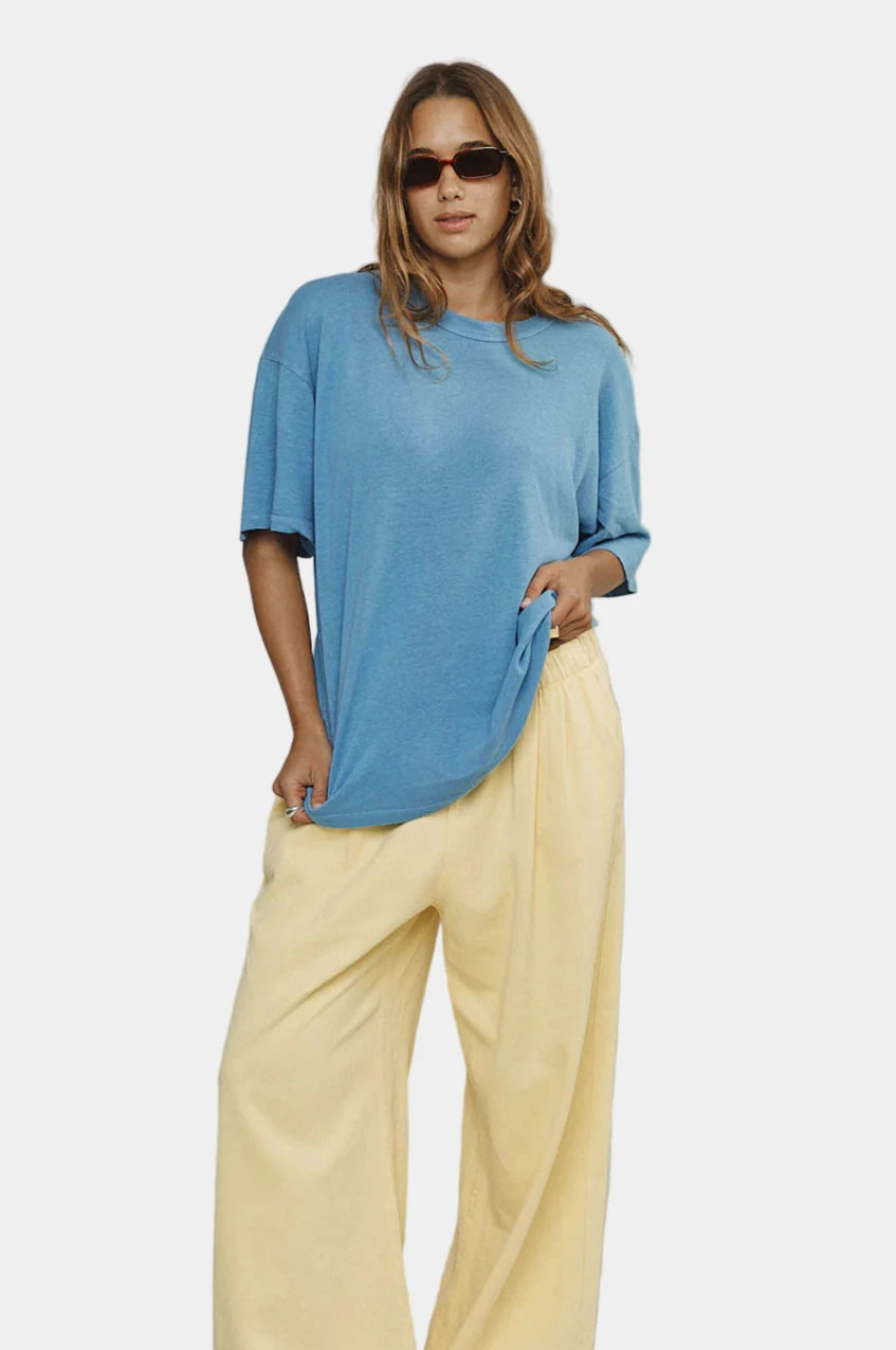 Woman wearing a blue t-shirt and yellow pants against a plain background